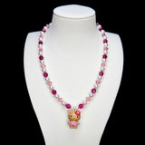 Detail product photo of a pink pearl cat charm necklace with white pearls, pink crystals, and gold-tone hardware.