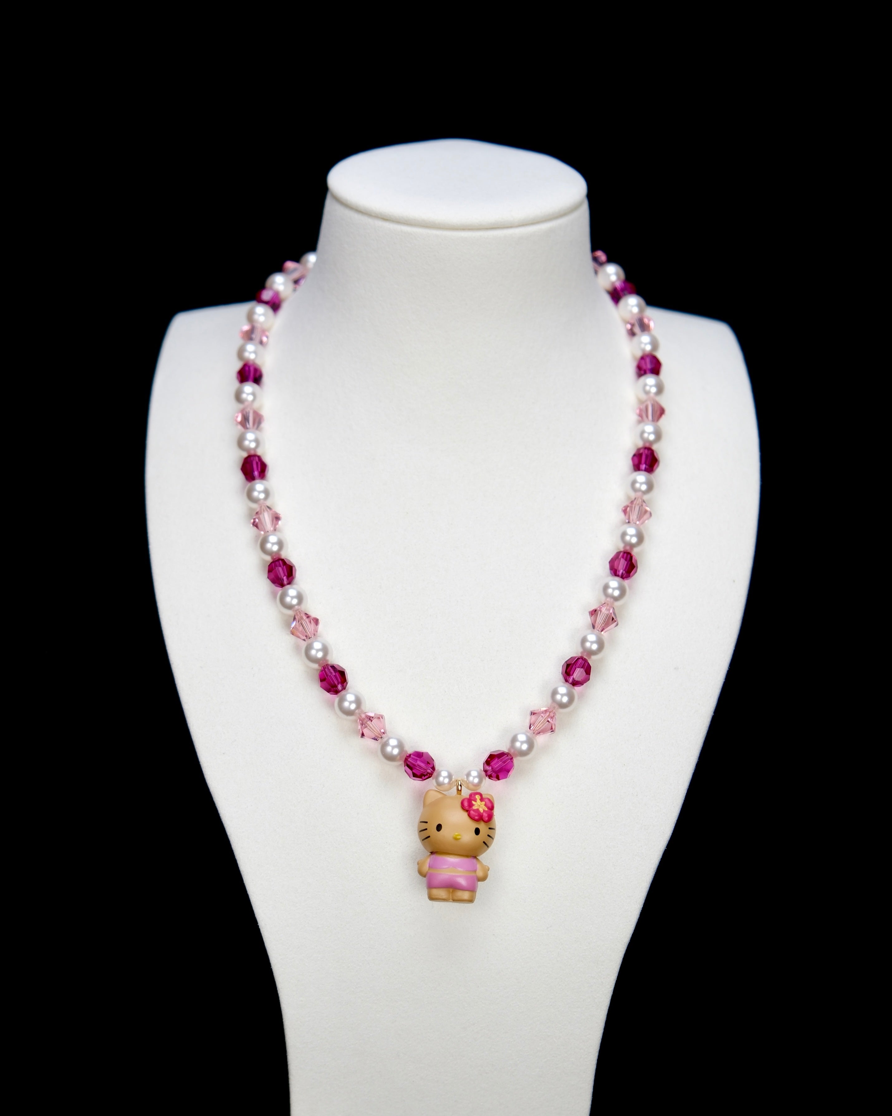 Detail product photo of a pink pearl cat charm necklace with white pearls, pink crystals, and gold-tone hardware.