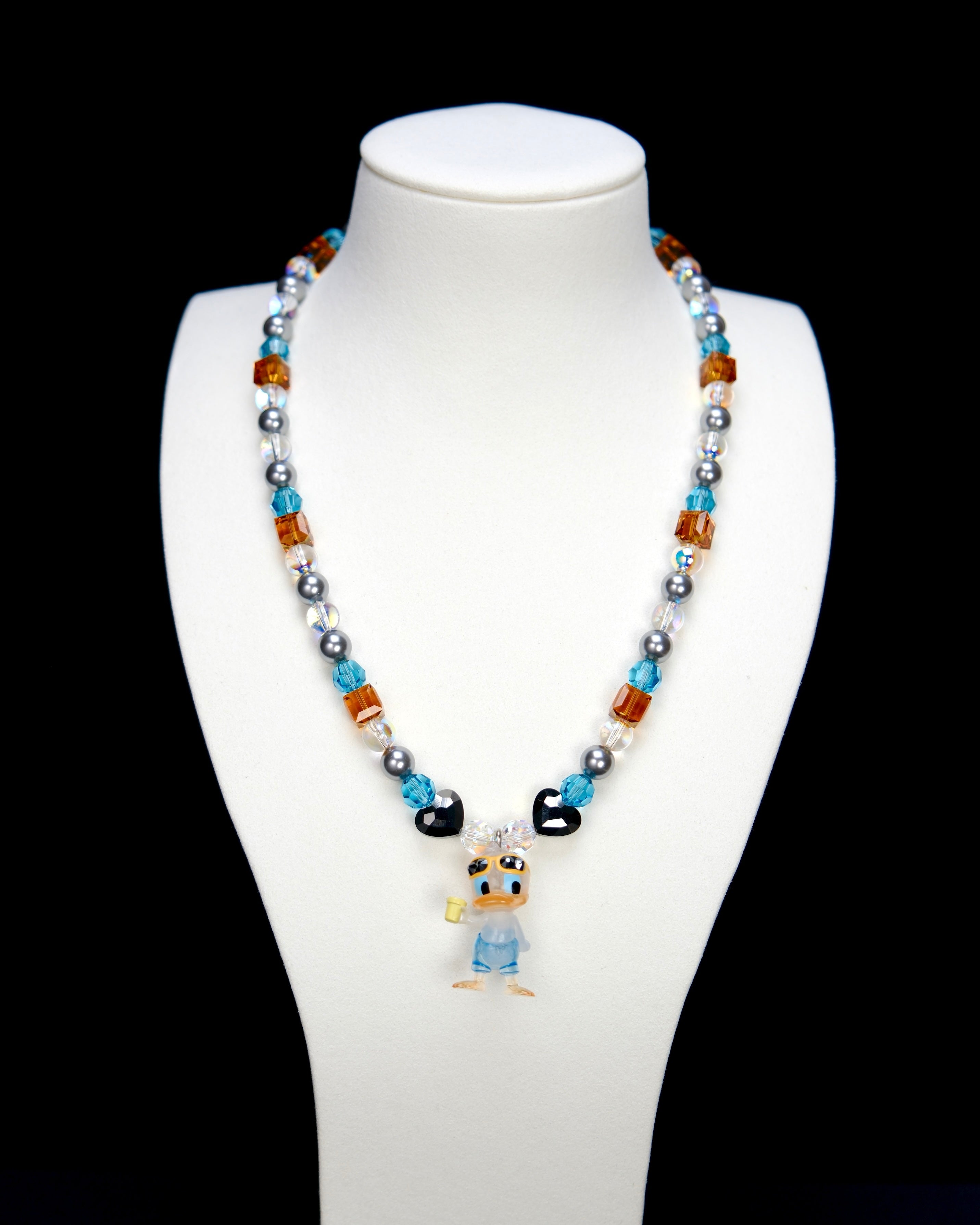 Detail product photo of an orange and blue duck charm necklace with gray pearls and faceted crystal beads.