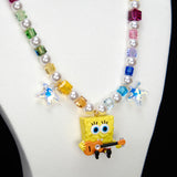 Detail product photo of a rainbow crystal and pearl guitar charm necklace with blue crystal star accents.