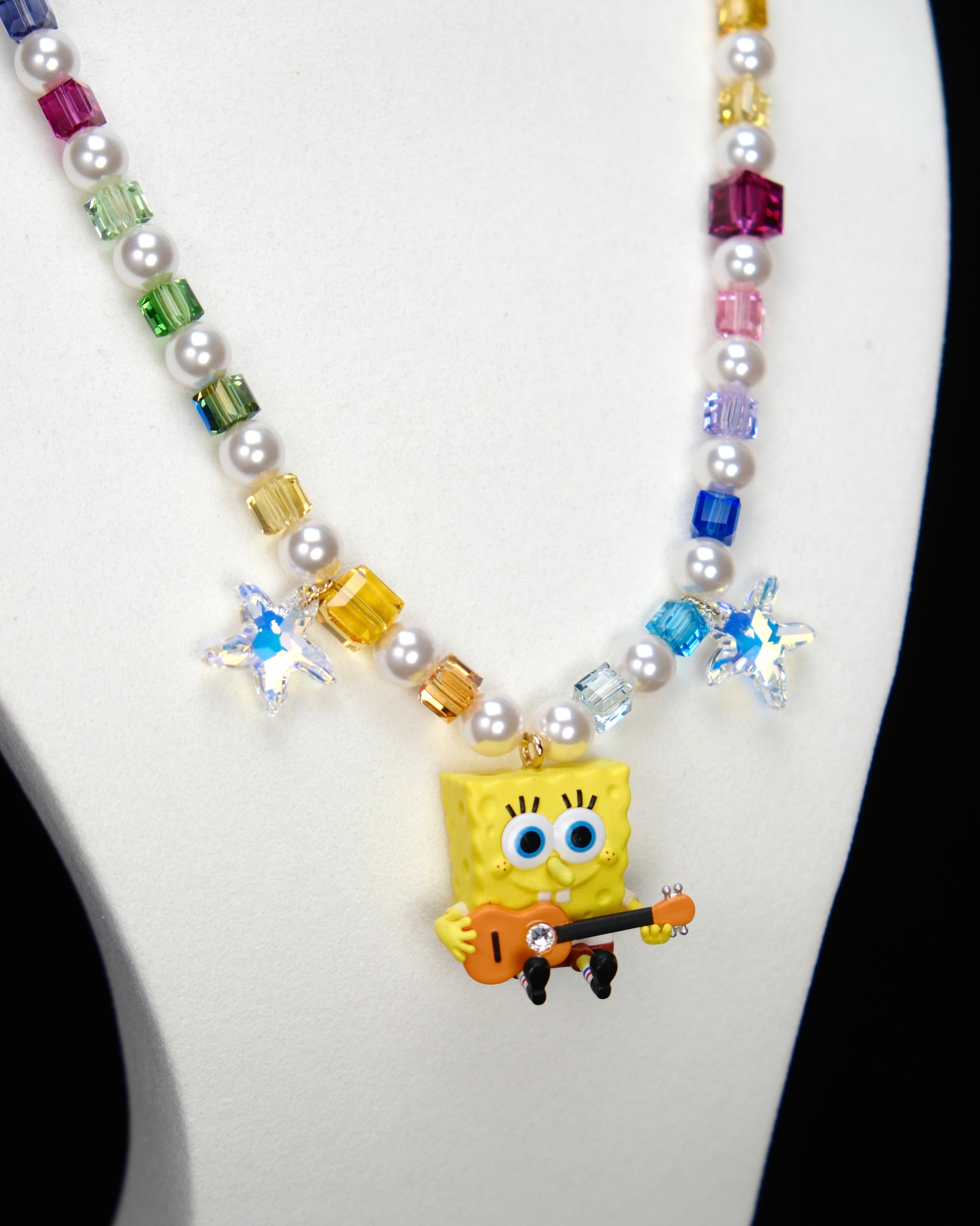 Detail product photo of a rainbow crystal and pearl guitar charm necklace with blue crystal star accents.