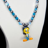 Detail product photo of a blue crystal and charcoal pearl charm necklace with a vintage yellow character charm.