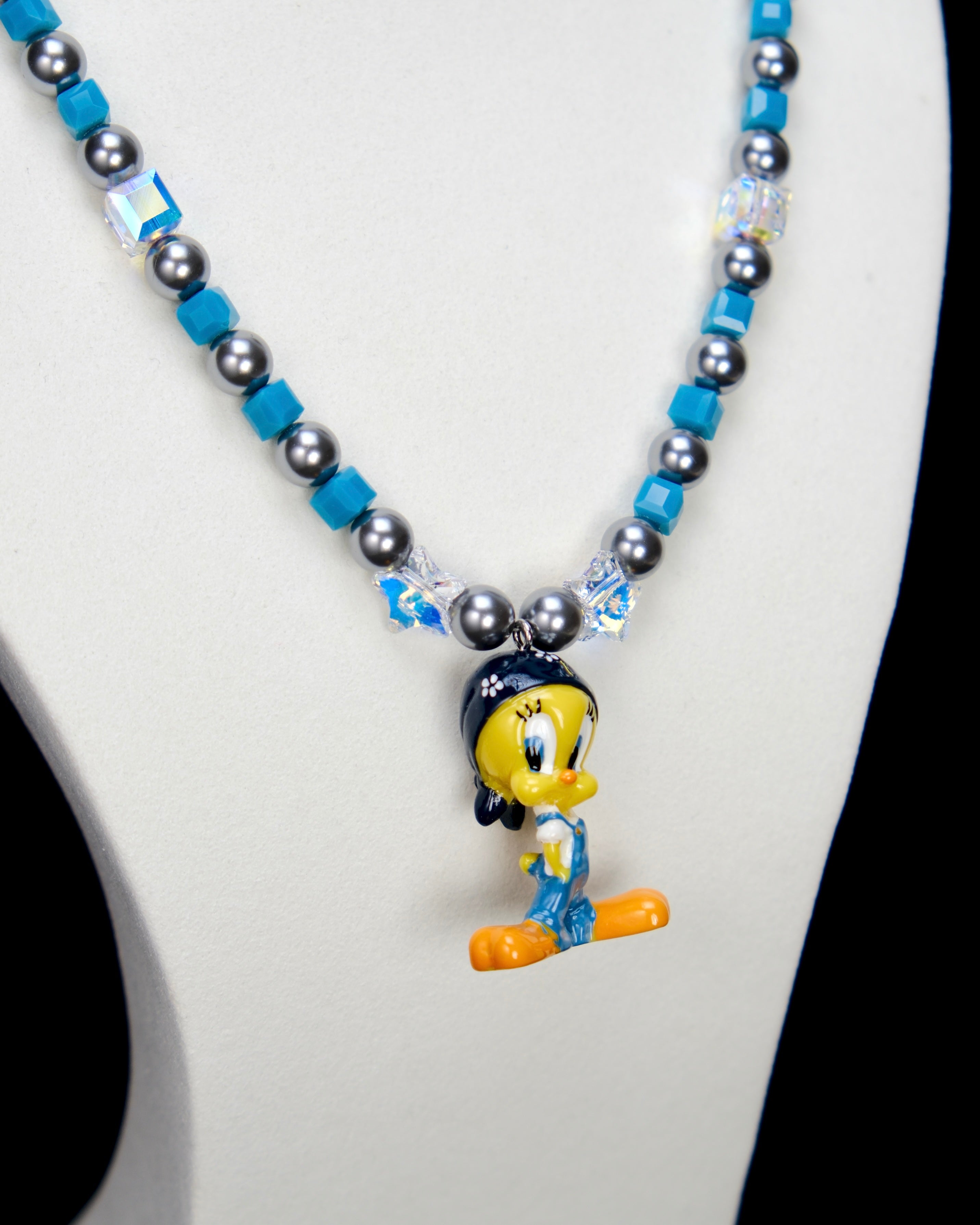 Detail product photo of a blue crystal and charcoal pearl charm necklace with a vintage yellow character charm.