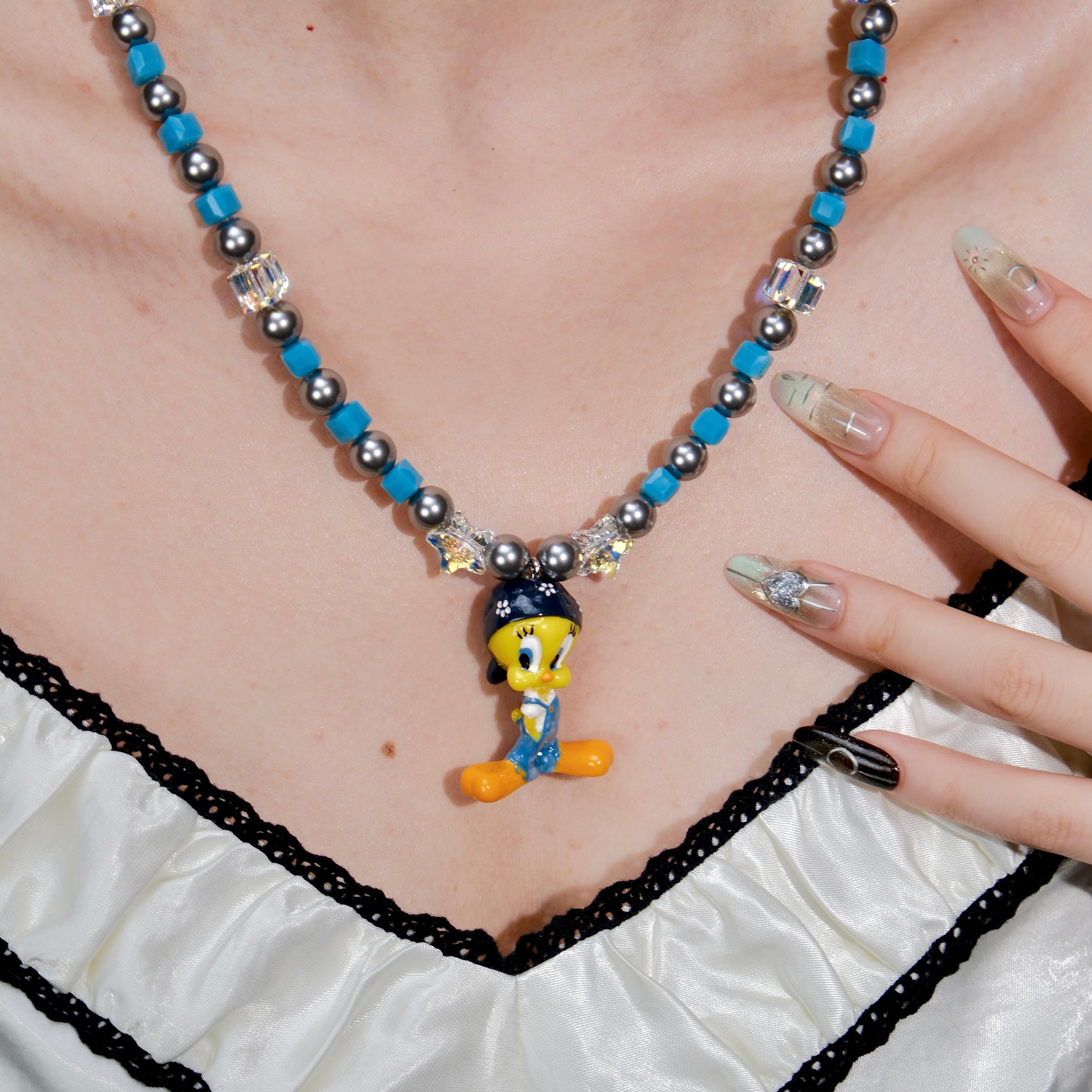 Product photo of a blue crystal and charcoal pearl charm necklace with a vintage yellow character charm.