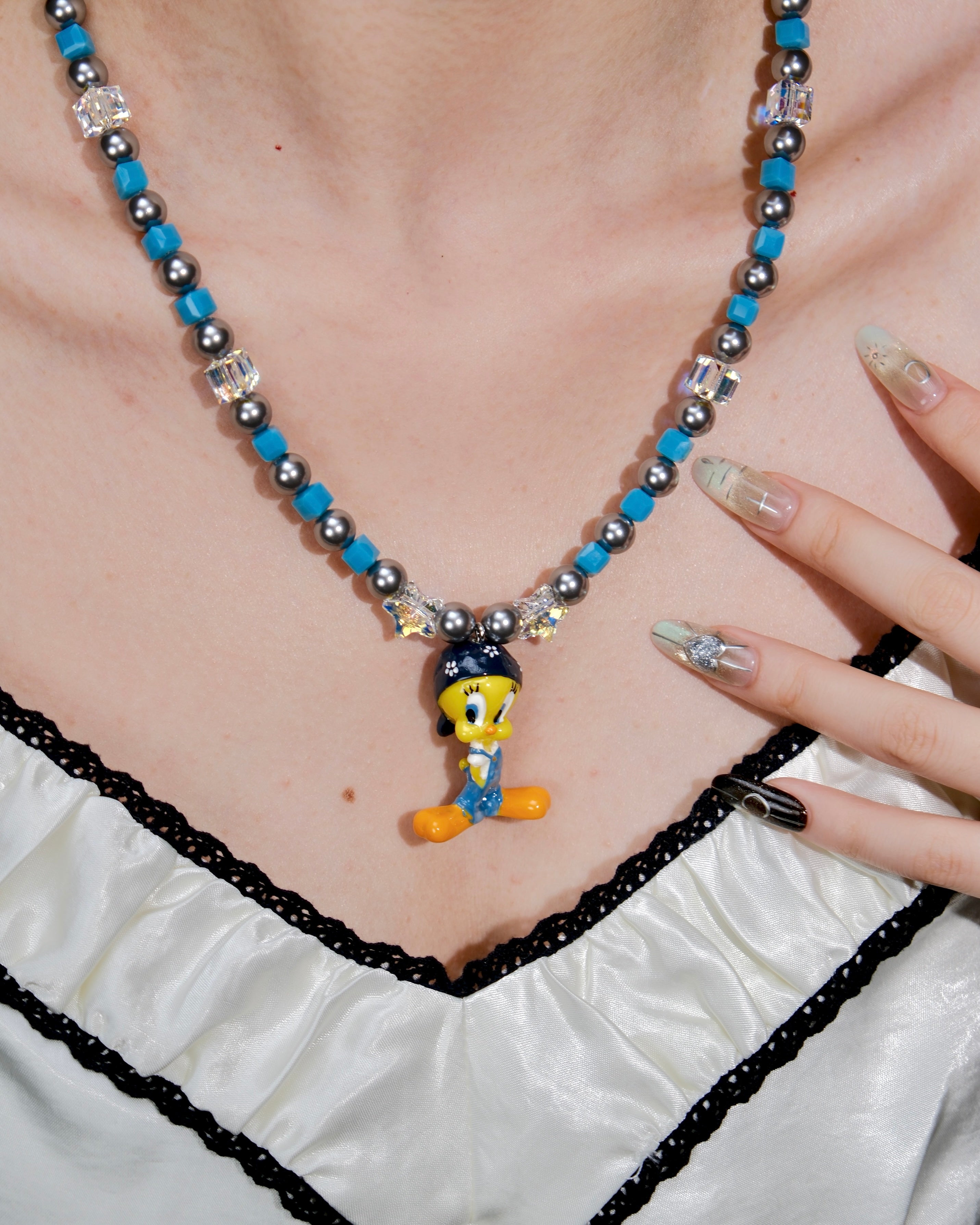 Product photo of a blue crystal and charcoal pearl charm necklace with a vintage yellow character charm.