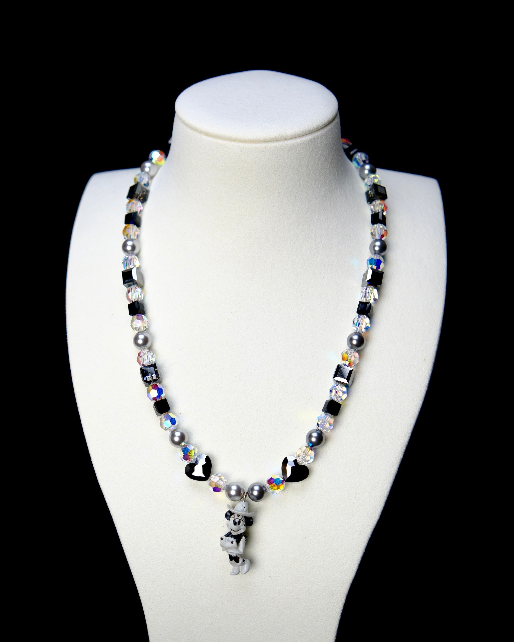Front studio product view of Midnight Magic Crystal Charm Necklace on a white jewelry display against a black background.