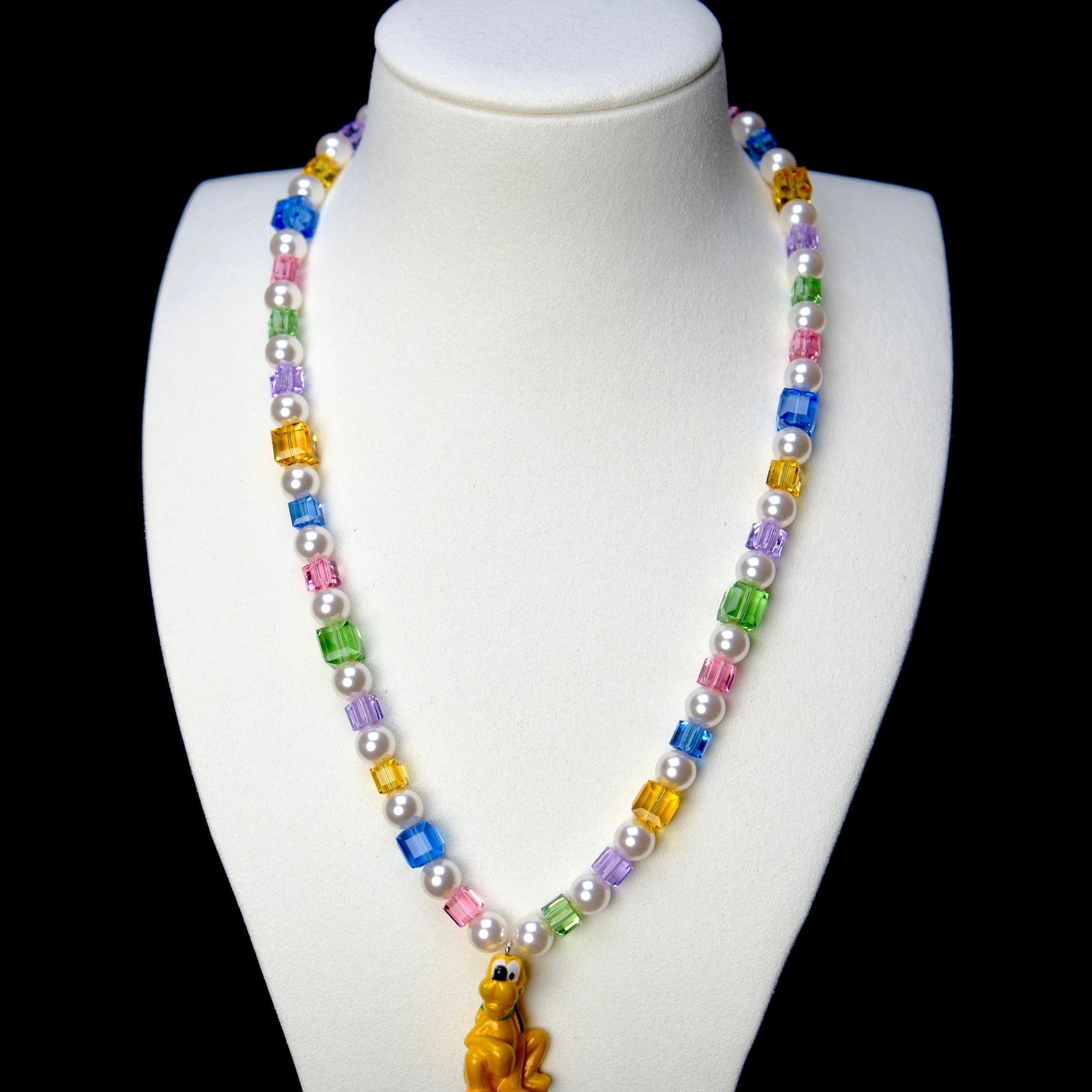 Front studio product view of Rainbow Daydream Crystal Charm Necklace on a white jewelry display against a black background.