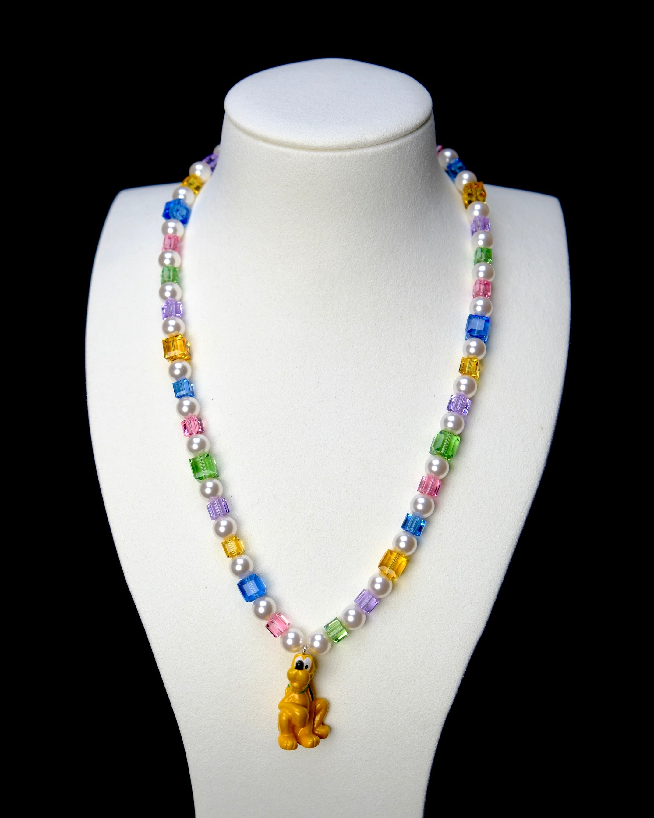 Front studio product view of Rainbow Daydream Crystal Charm Necklace on a white jewelry display against a black background.