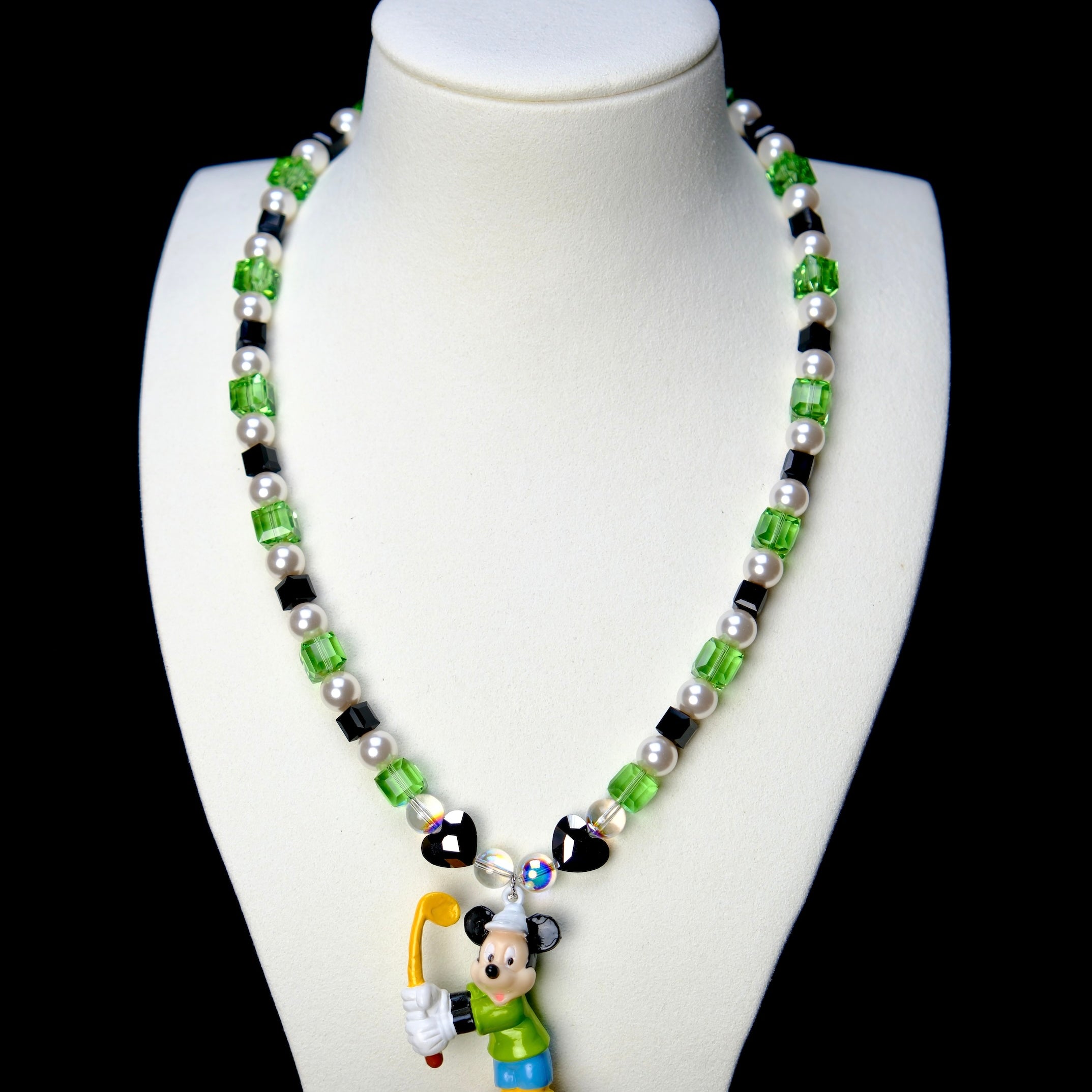 Front studio product view of Emerald Quest Crystal Charm Necklace on a white jewelry display against a black background.