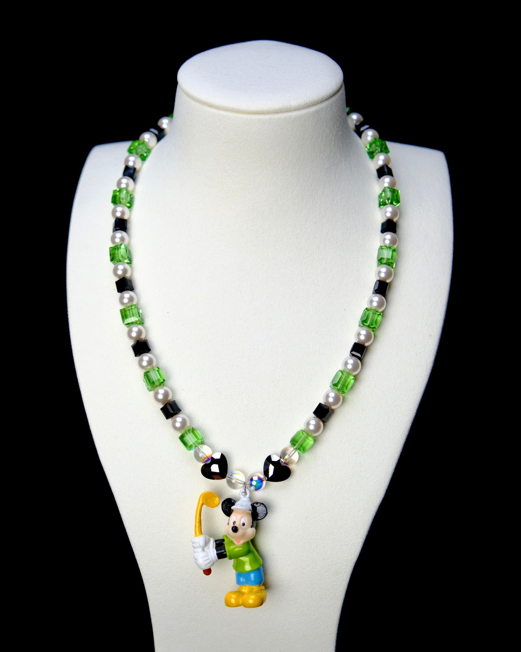 Front studio product view of Emerald Quest Crystal Charm Necklace on a white jewelry display against a black background.