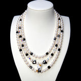 Front studio product view of Monochrome Pearl Triple Layer Necklace on a white jewelry display against a black background.