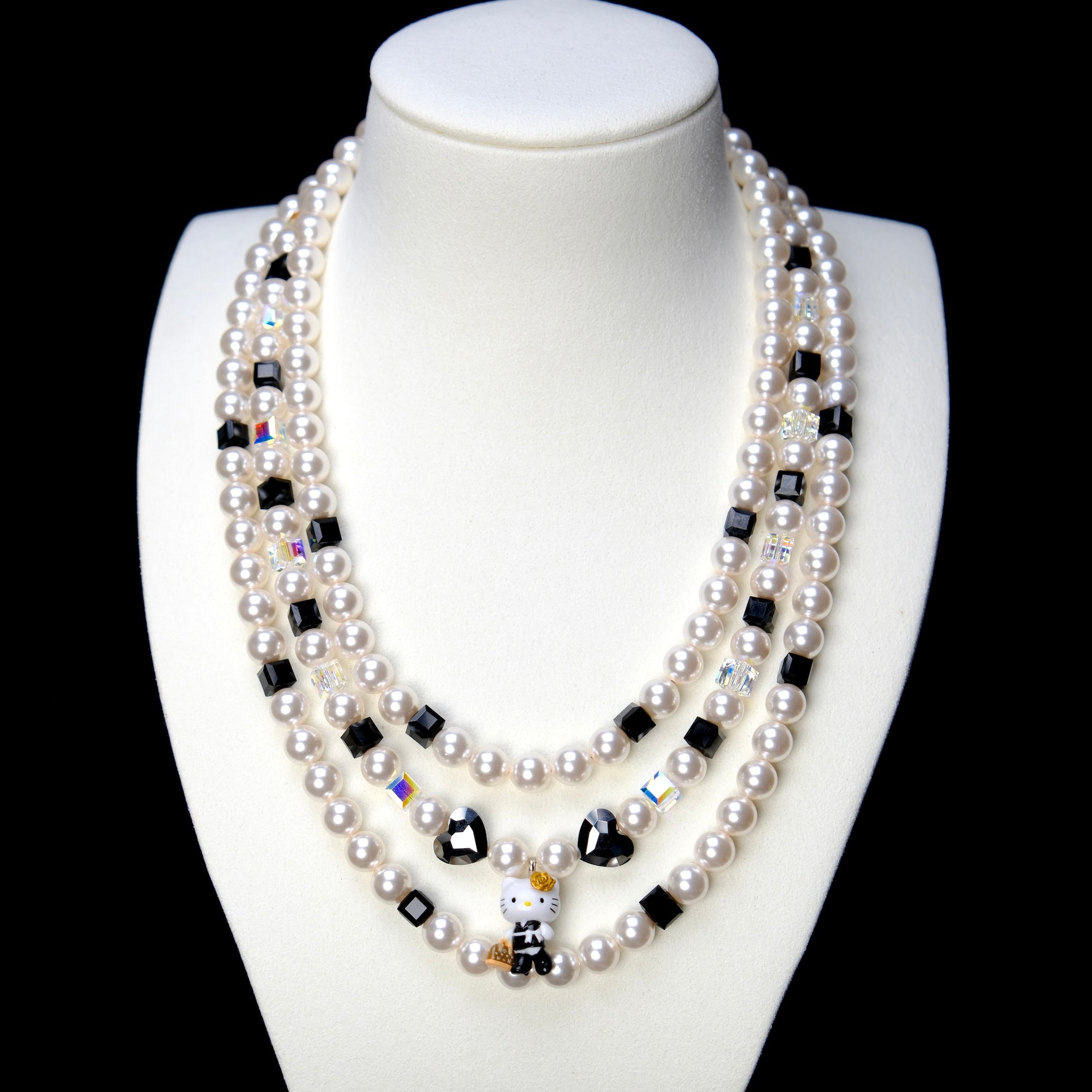 Front studio product view of Monochrome Pearl Triple Layer Necklace on a white jewelry display against a black background.
