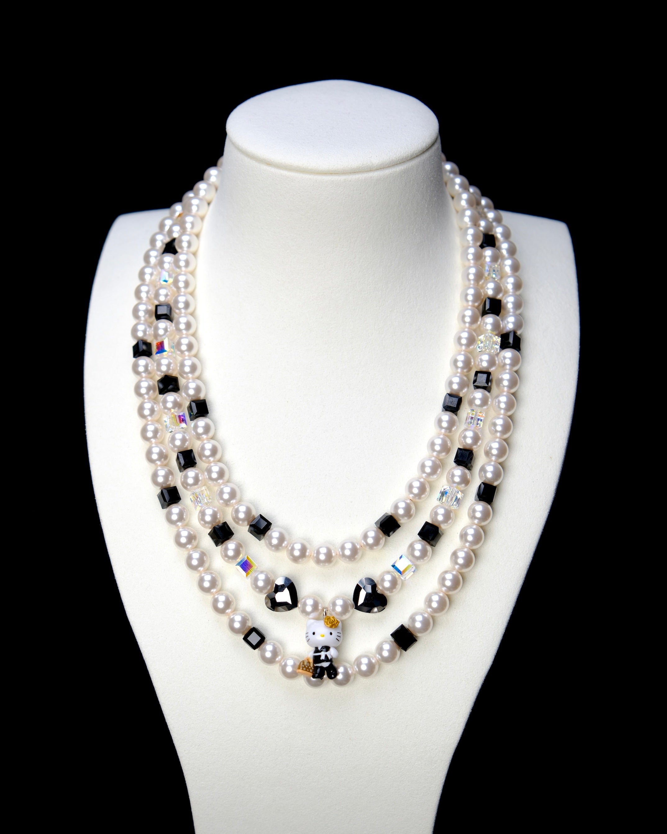 Front studio product view of Monochrome Pearl Triple Layer Necklace on a white jewelry display against a black background.