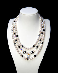 Front studio product view of Monochrome Pearl Triple Layer Necklace on a white jewelry display against a black background.