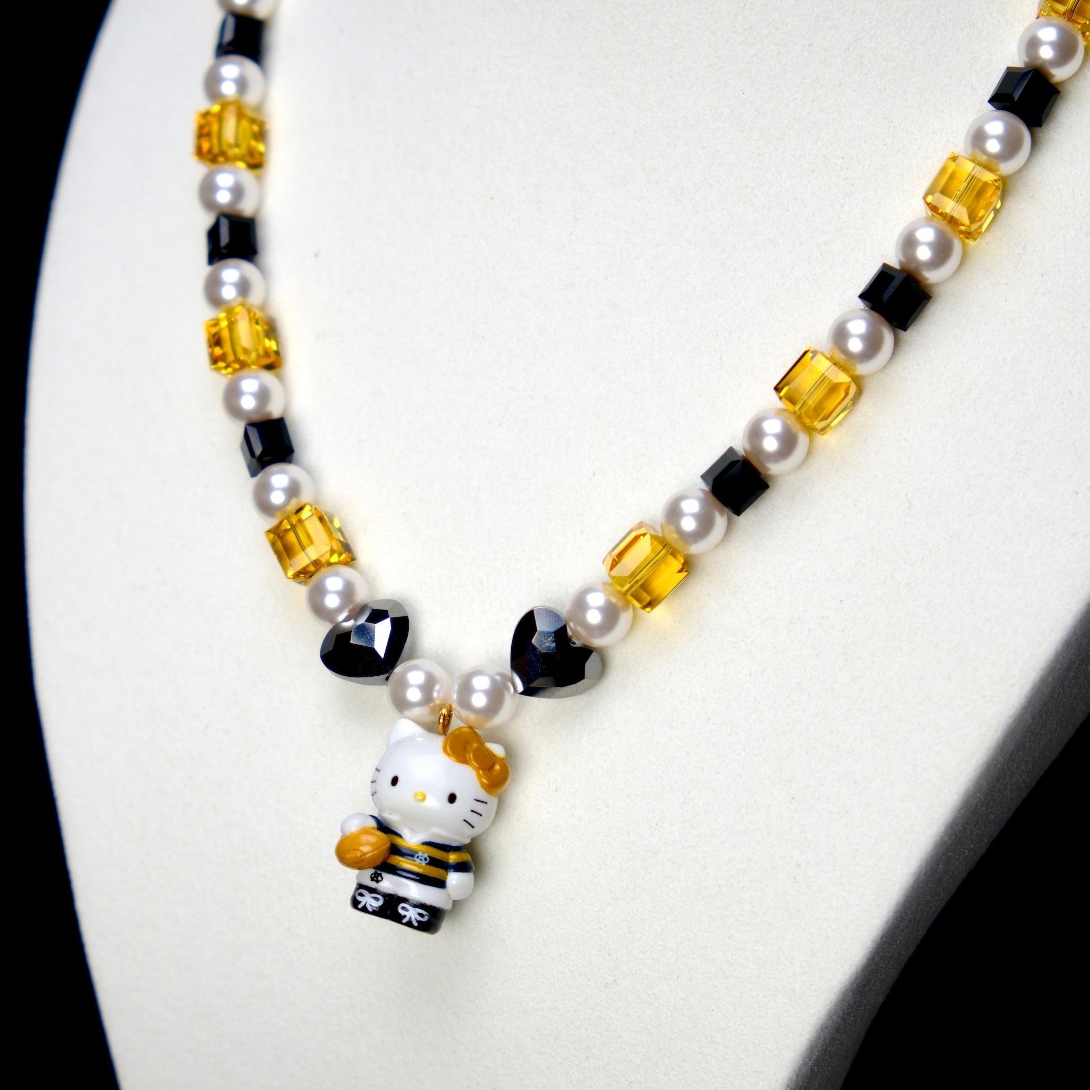 Angled studio product view of Golden Voyage Crystal Charm Necklace on a white jewelry display against a black background.