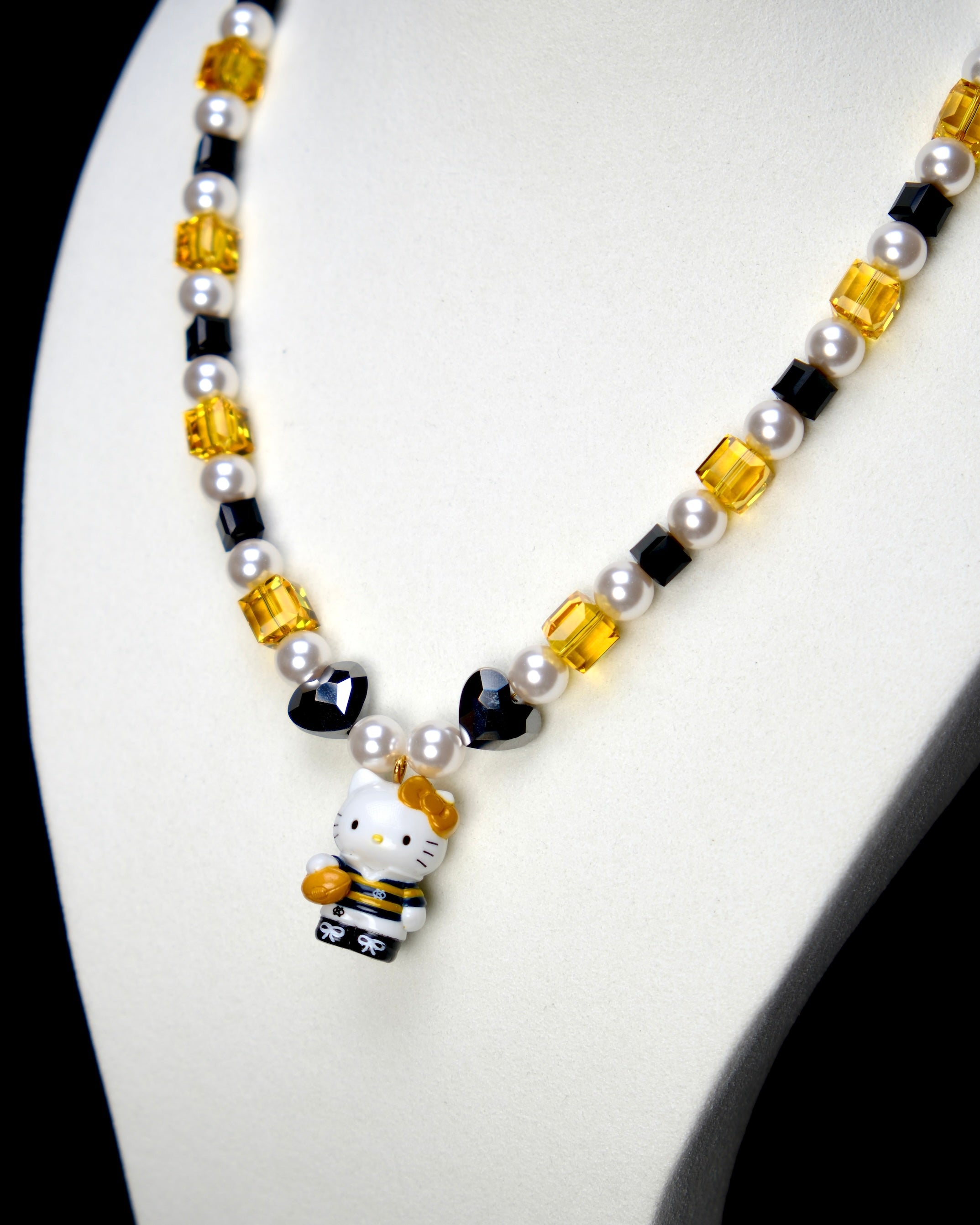 Angled studio product view of Golden Voyage Crystal Charm Necklace on a white jewelry display against a black background.