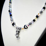 Angled studio product view of Midnight Magic Crystal Charm Necklace on a white jewelry display against a black background.