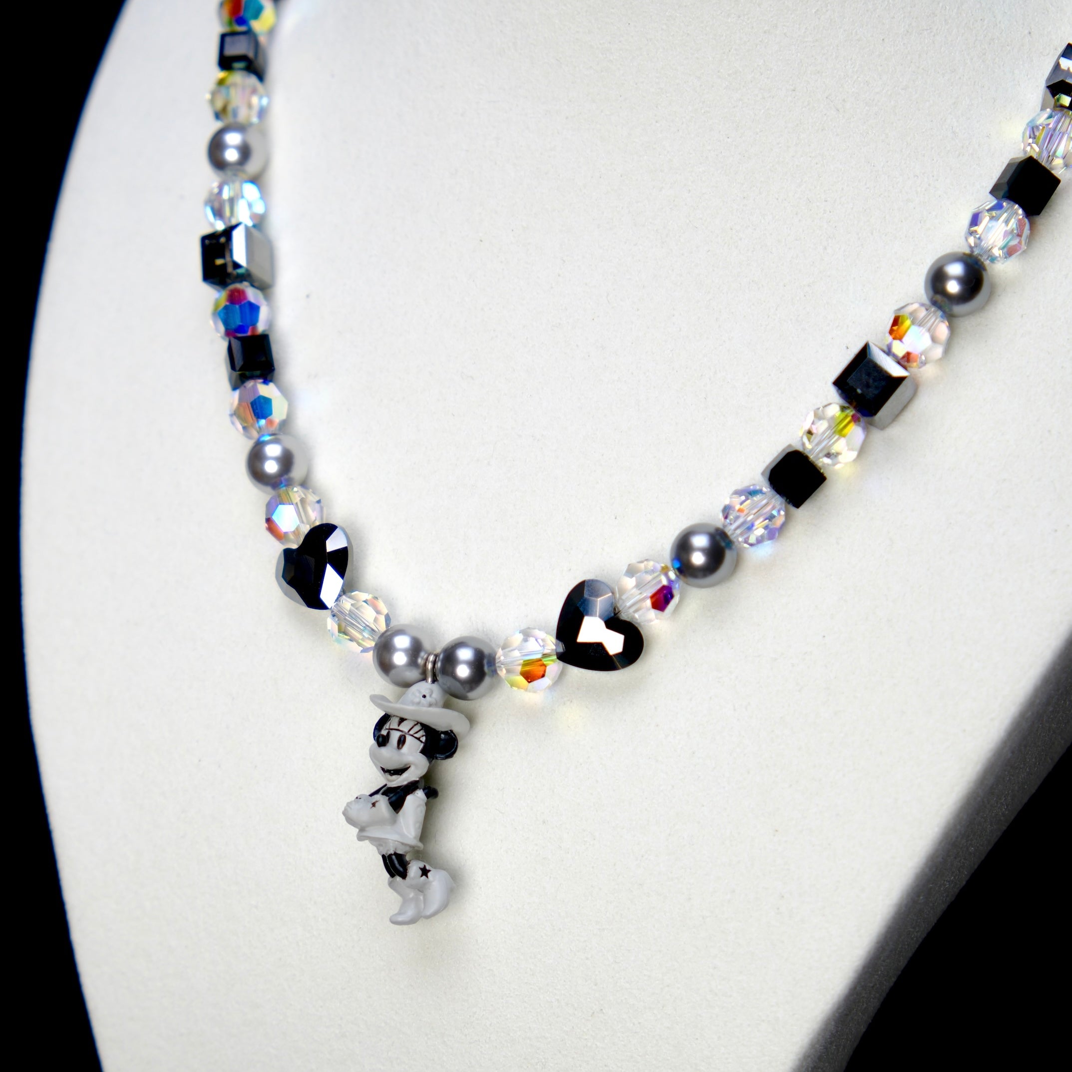 Angled studio product view of Midnight Magic Crystal Charm Necklace on a white jewelry display against a black background.