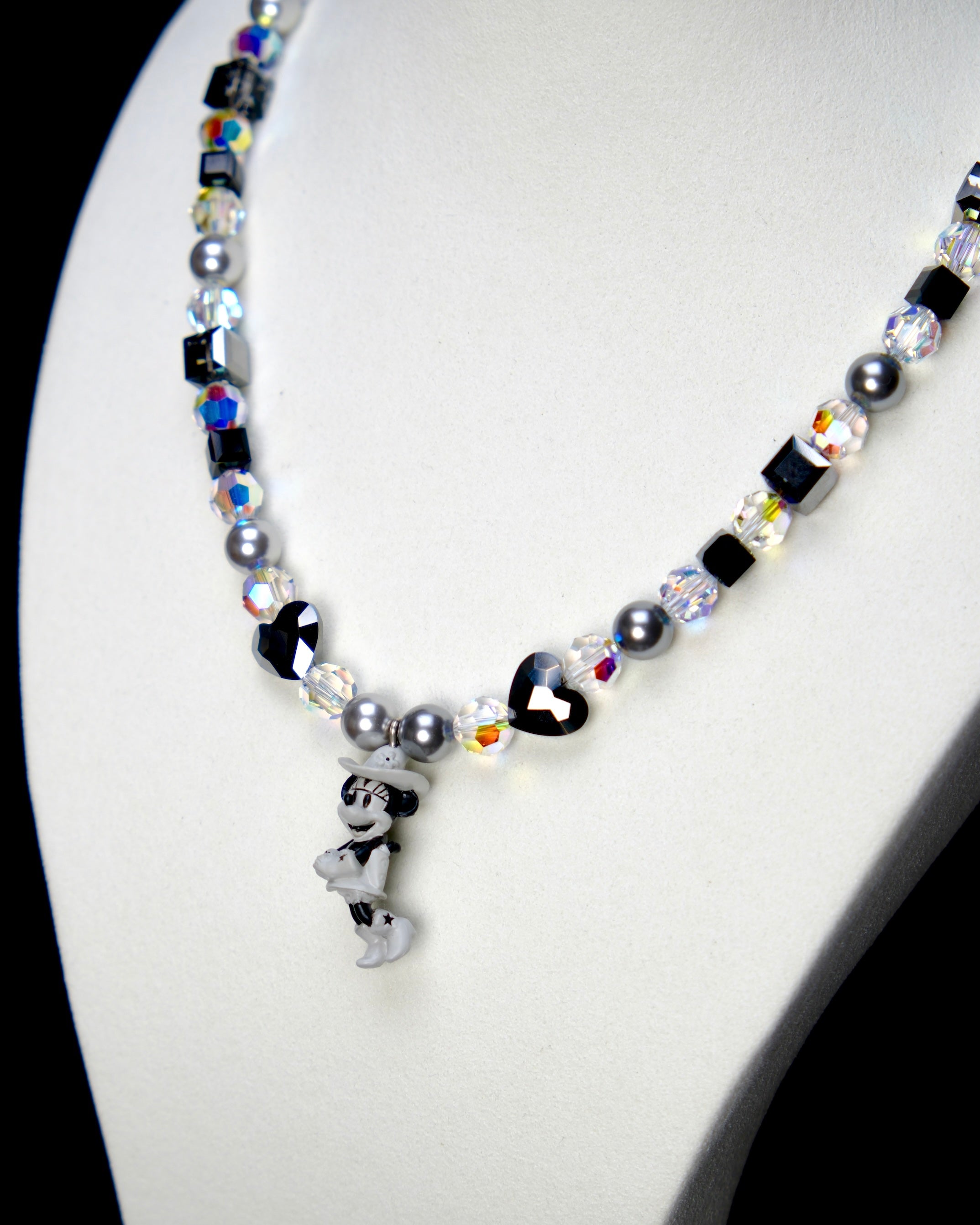 Angled studio product view of Midnight Magic Crystal Charm Necklace on a white jewelry display against a black background.
