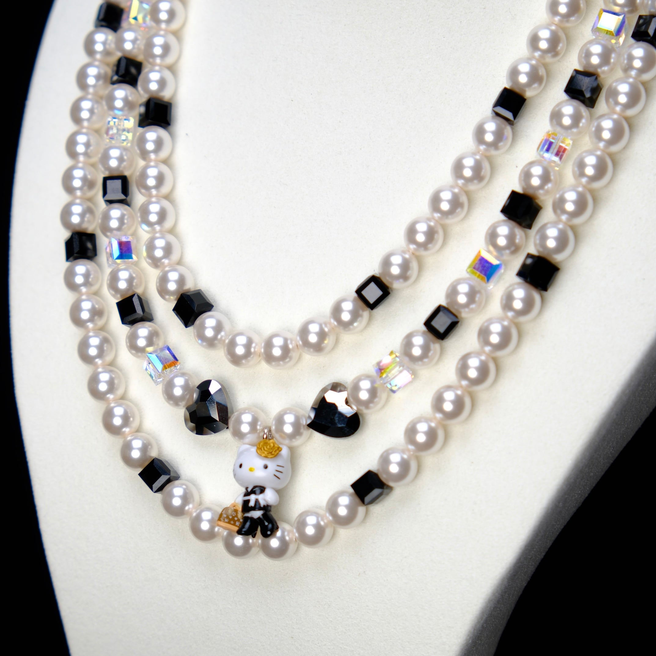 Angled studio product view of Monochrome Pearl Triple Layer Necklace on a white jewelry display against a black background.