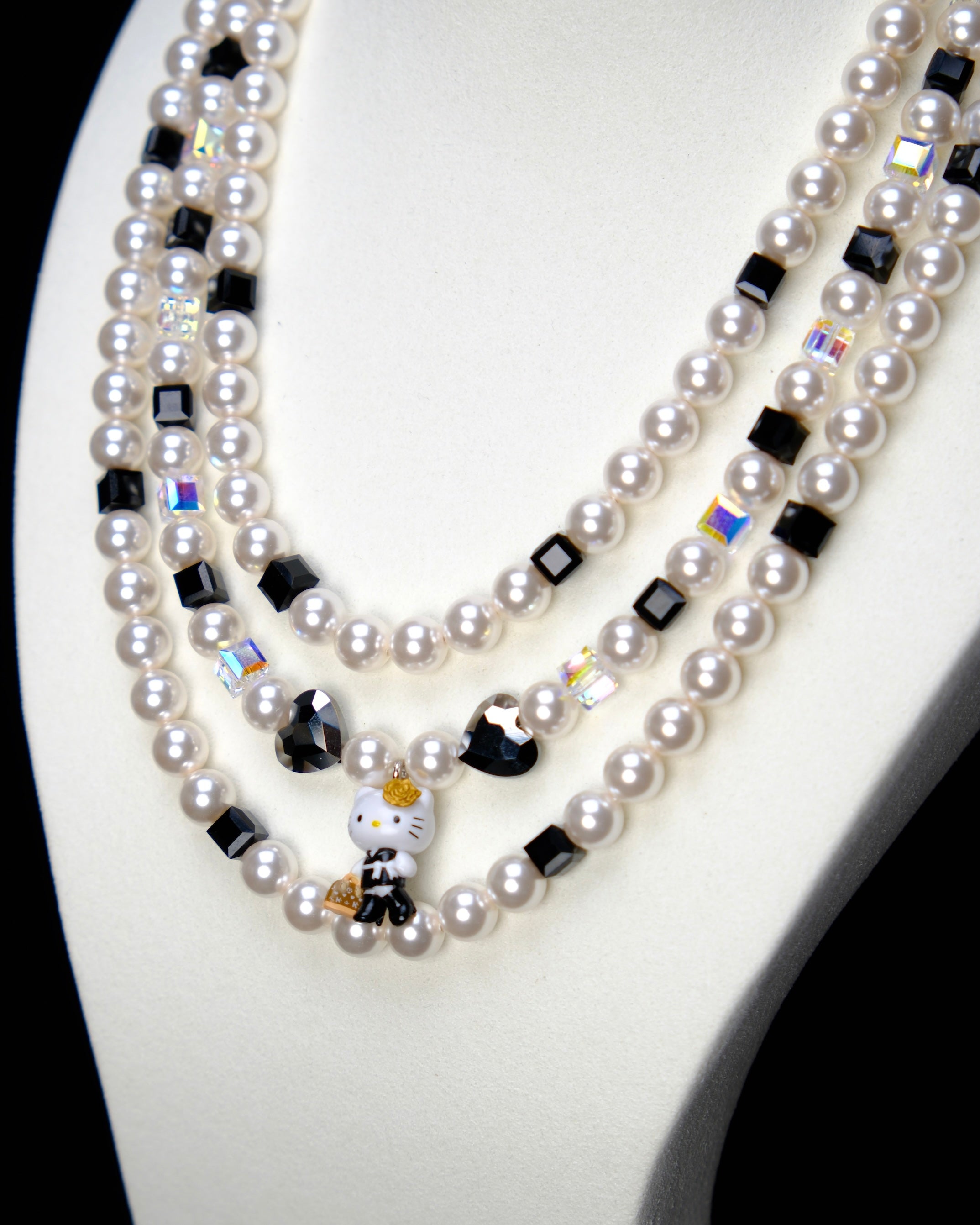 Angled studio product view of Monochrome Pearl Triple Layer Necklace on a white jewelry display against a black background.