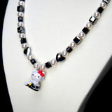 Angled studio product view of Noir Court Crystal Charm Necklace on a white jewelry display against a black background.