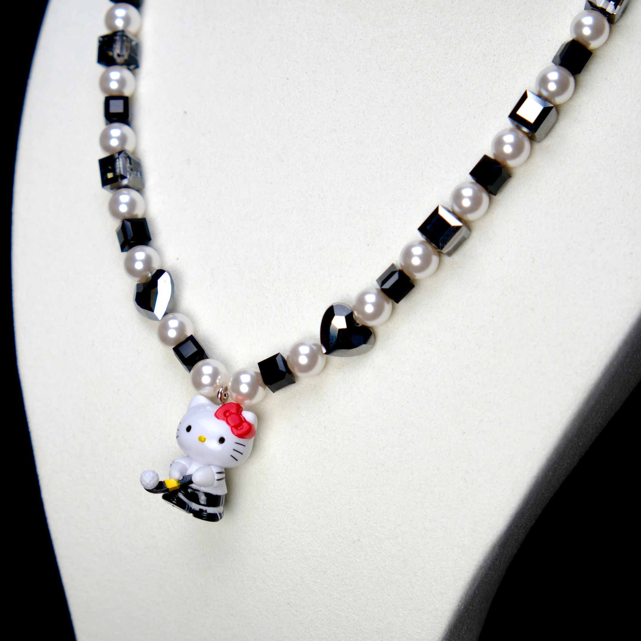 Angled studio product view of Noir Court Crystal Charm Necklace on a white jewelry display against a black background.