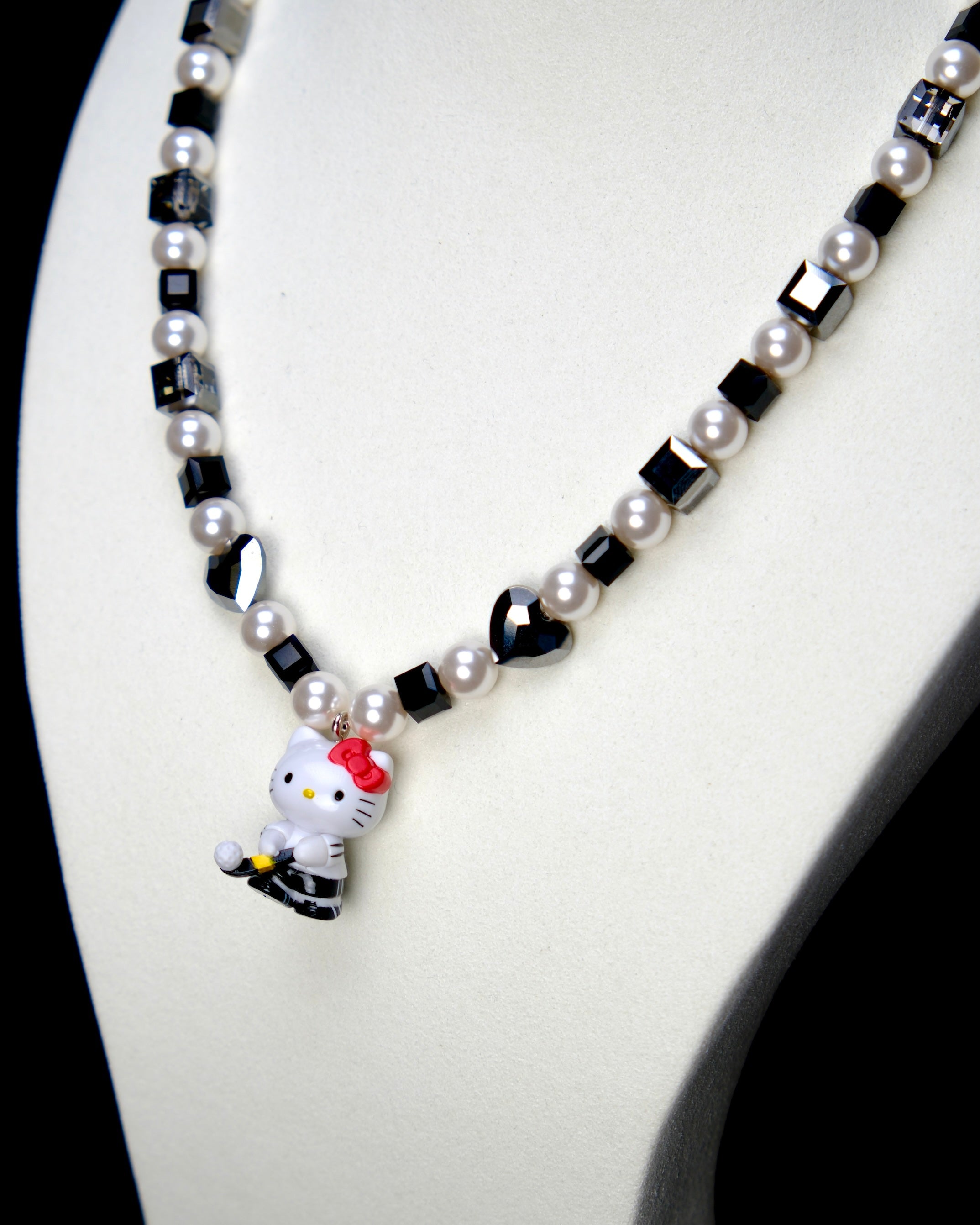 Angled studio product view of Noir Court Crystal Charm Necklace on a white jewelry display against a black background.