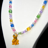 Angled studio product view of Rainbow Daydream Crystal Charm Necklace on a white jewelry display against a black background.