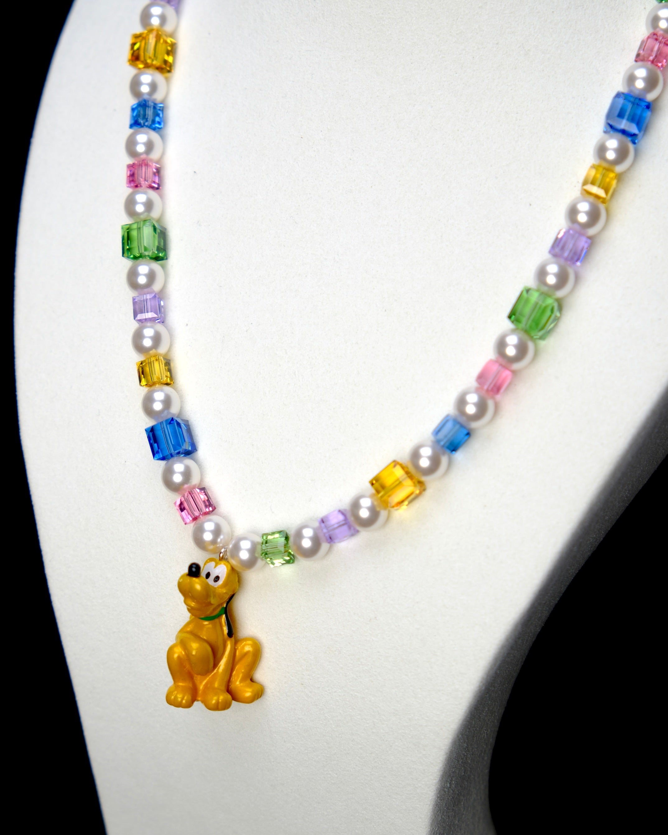 Angled studio product view of Rainbow Daydream Crystal Charm Necklace on a white jewelry display against a black background.