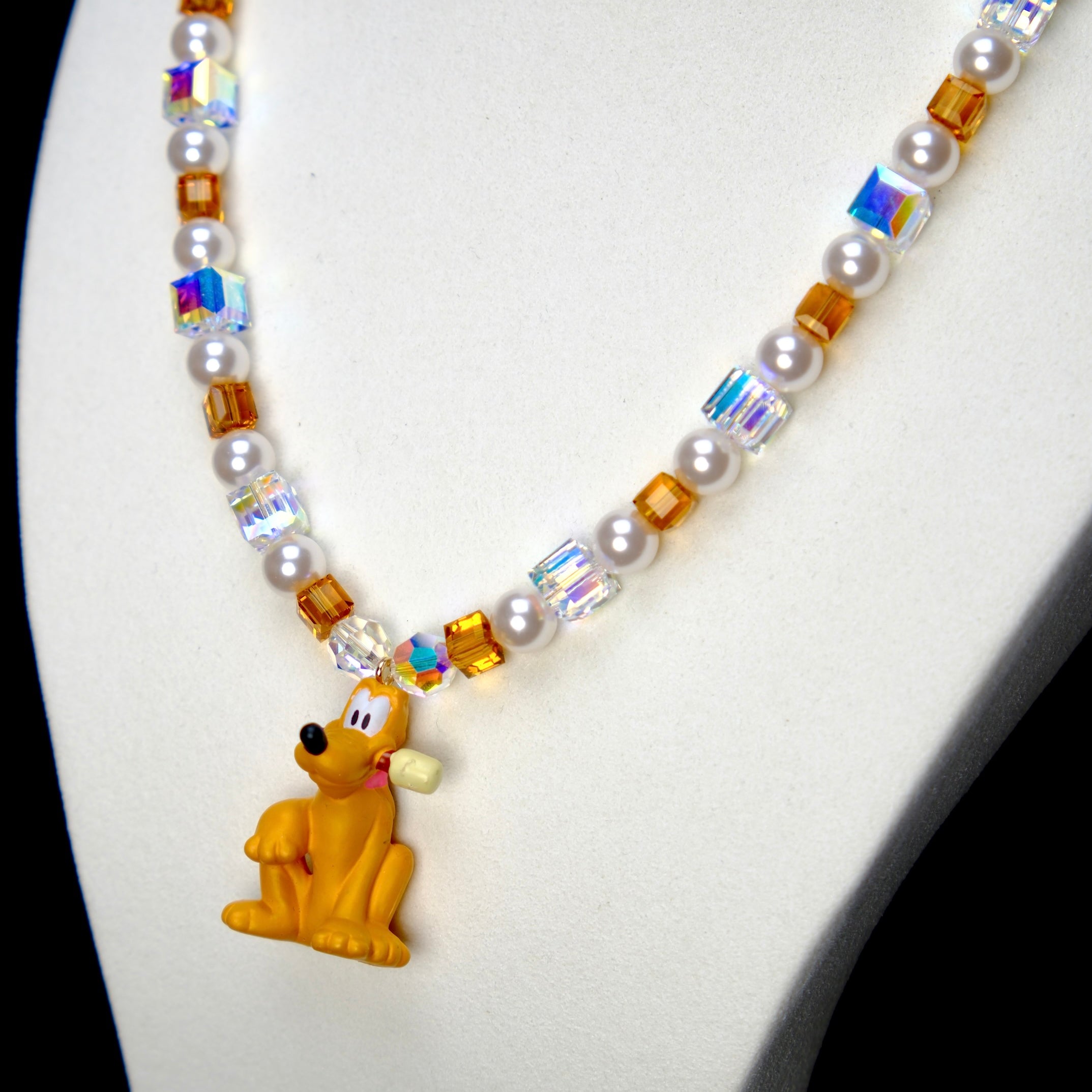 Angled studio product view of Amber Daydream Crystal Charm Necklace on a white jewelry display against a black background.