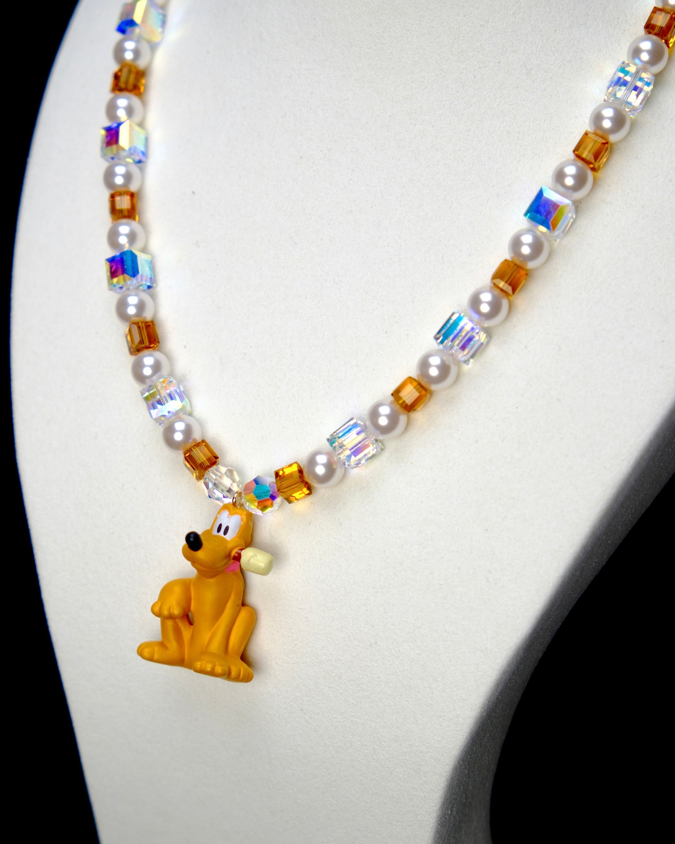 Angled studio product view of Amber Daydream Crystal Charm Necklace on a white jewelry display against a black background.