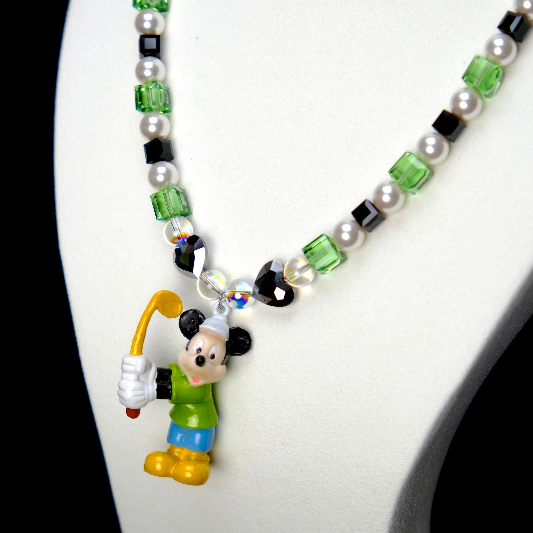 Angled studio product view of Emerald Quest Crystal Charm Necklace on a white jewelry display against a black background.