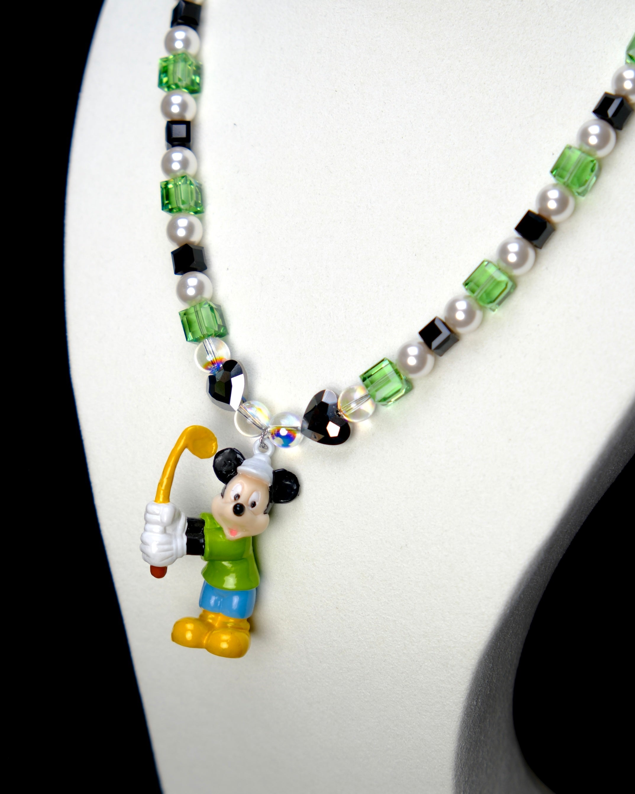 Angled studio product view of Emerald Quest Crystal Charm Necklace on a white jewelry display against a black background.