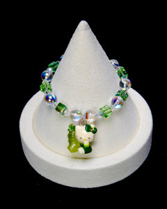 Green crystal cat charm bracelet with iridescent round beads and green cubes on a white display stand.