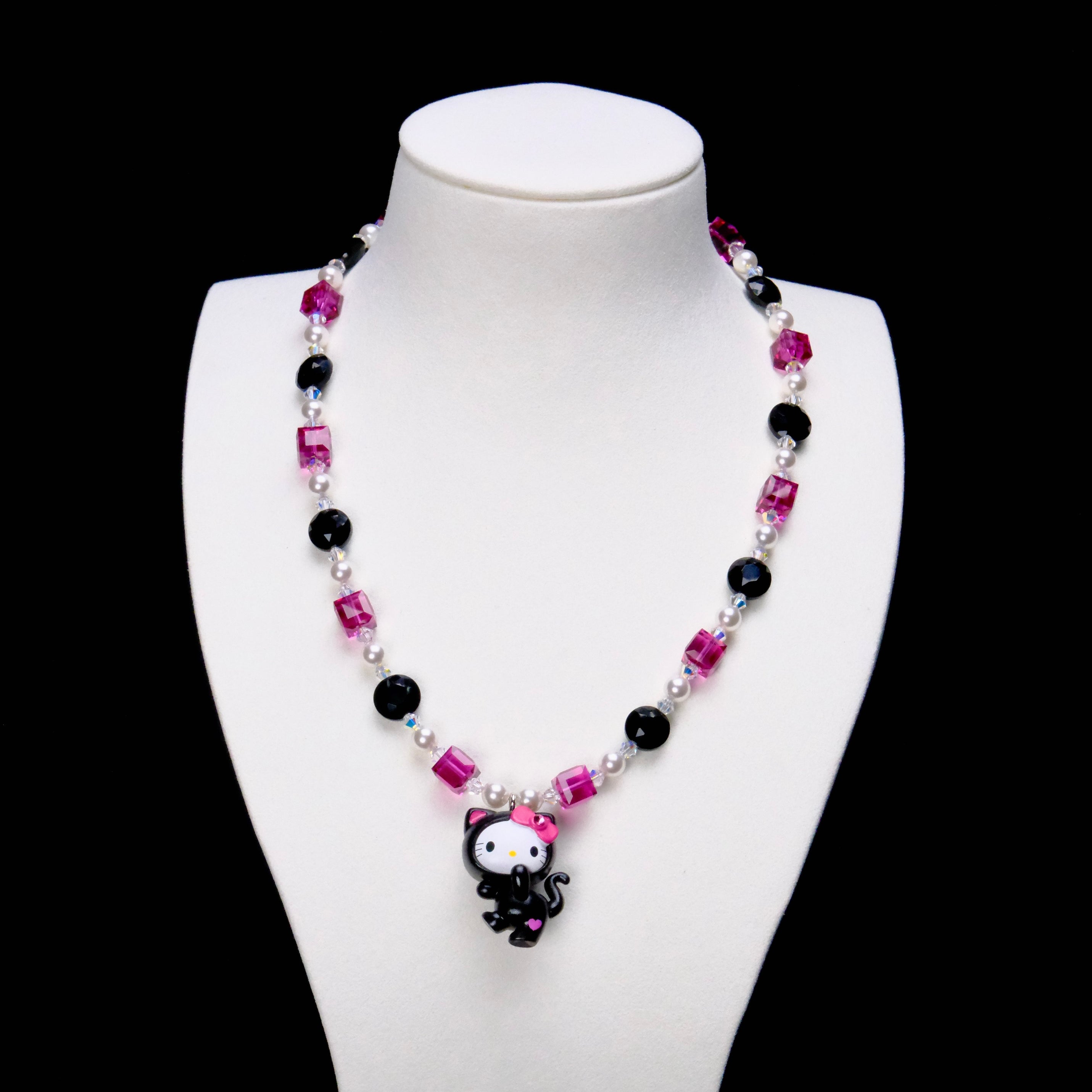Pink Noir Cat Charm Necklace with pink crystal cubes, black beads, white pearls and a black-costume cat pendant on a white bust.