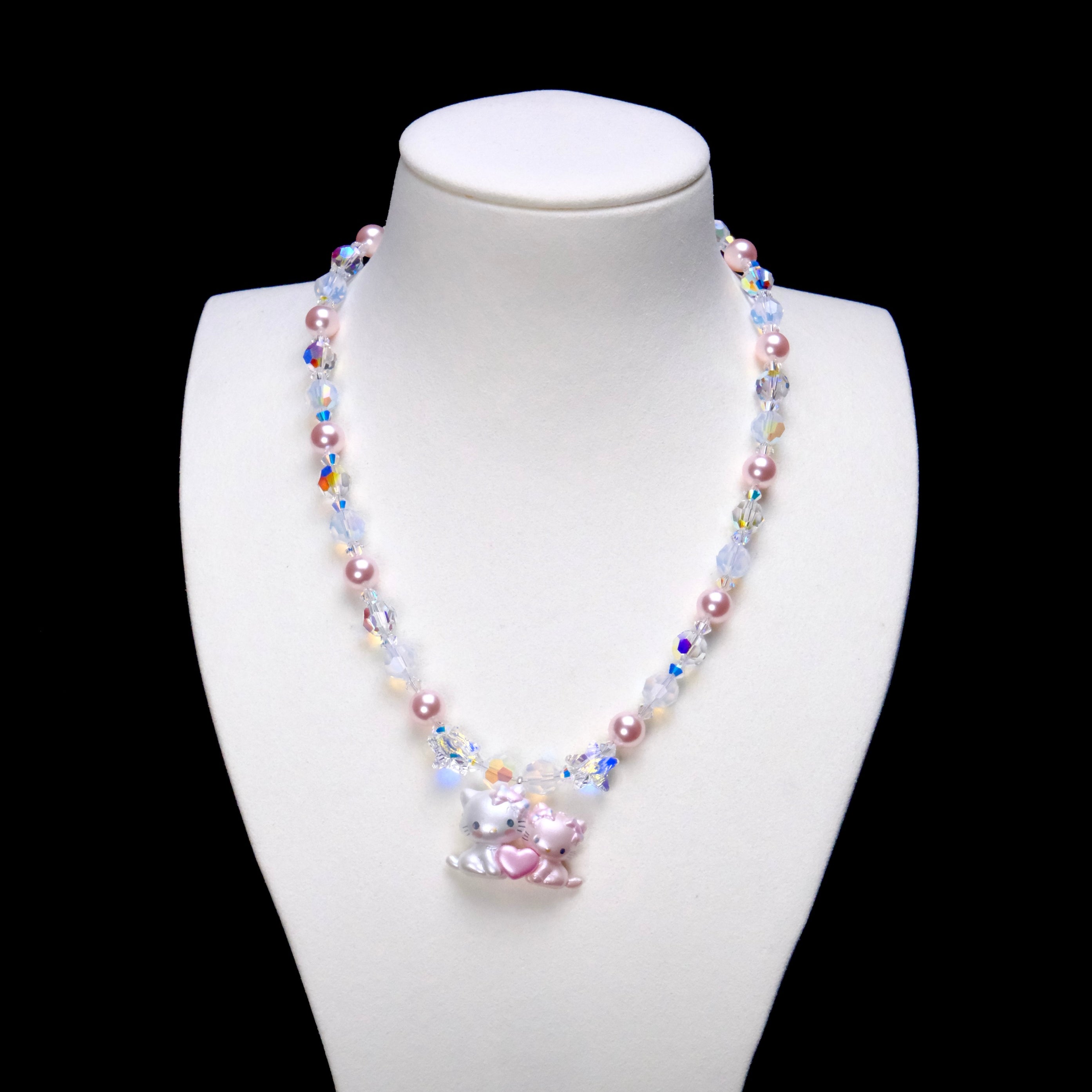 Sweethearts Cat Duo Necklace with pink pearls, iridescent crystals and a pink heart cat-pair pendant on a white bust.