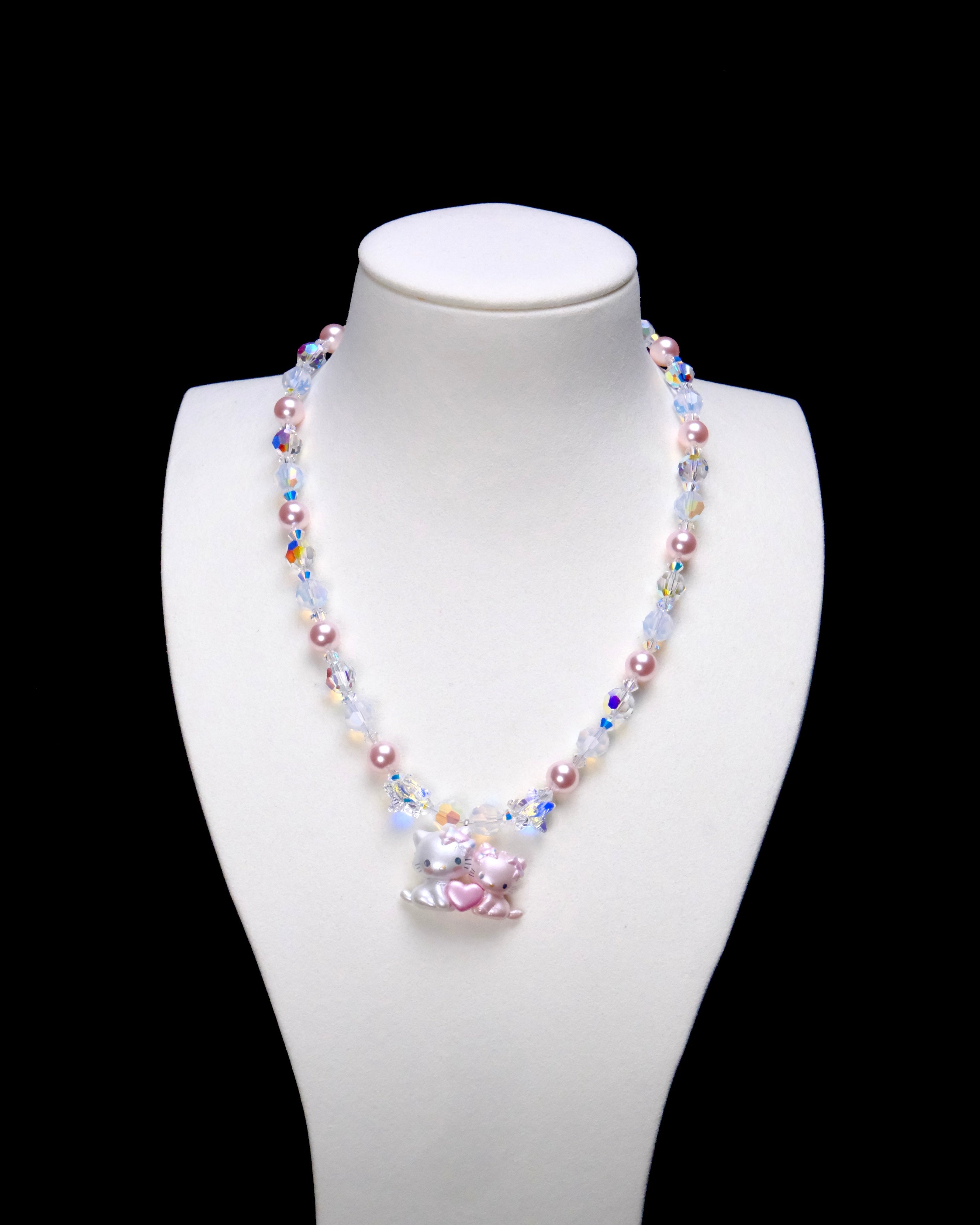 Sweethearts Cat Duo Necklace with pink pearls, iridescent crystals and a pink heart cat-pair pendant on a white bust.