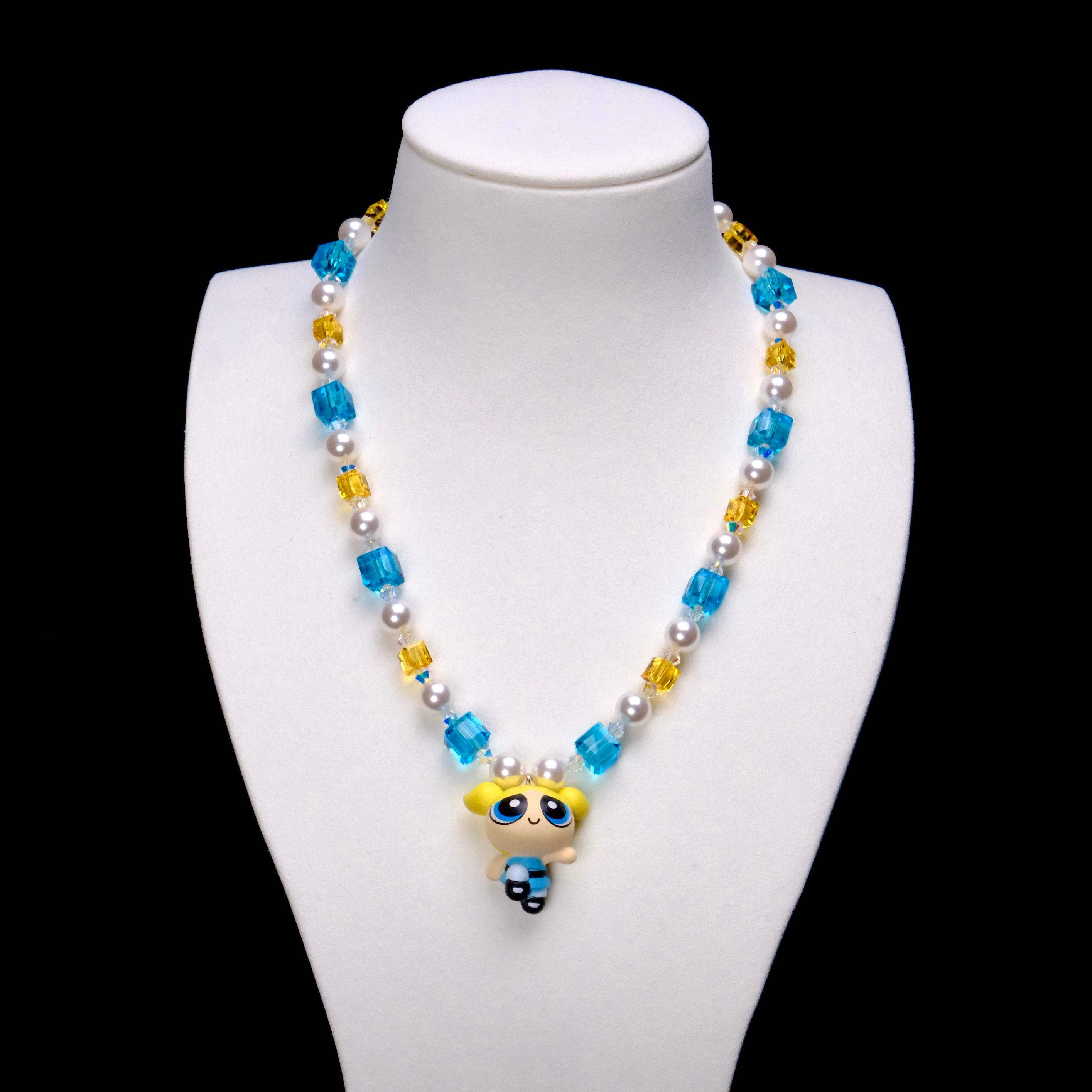 Blue Dreamer Charm Necklace with aqua and golden crystal cubes, white pearls and a blonde girl pendant on a white bust.