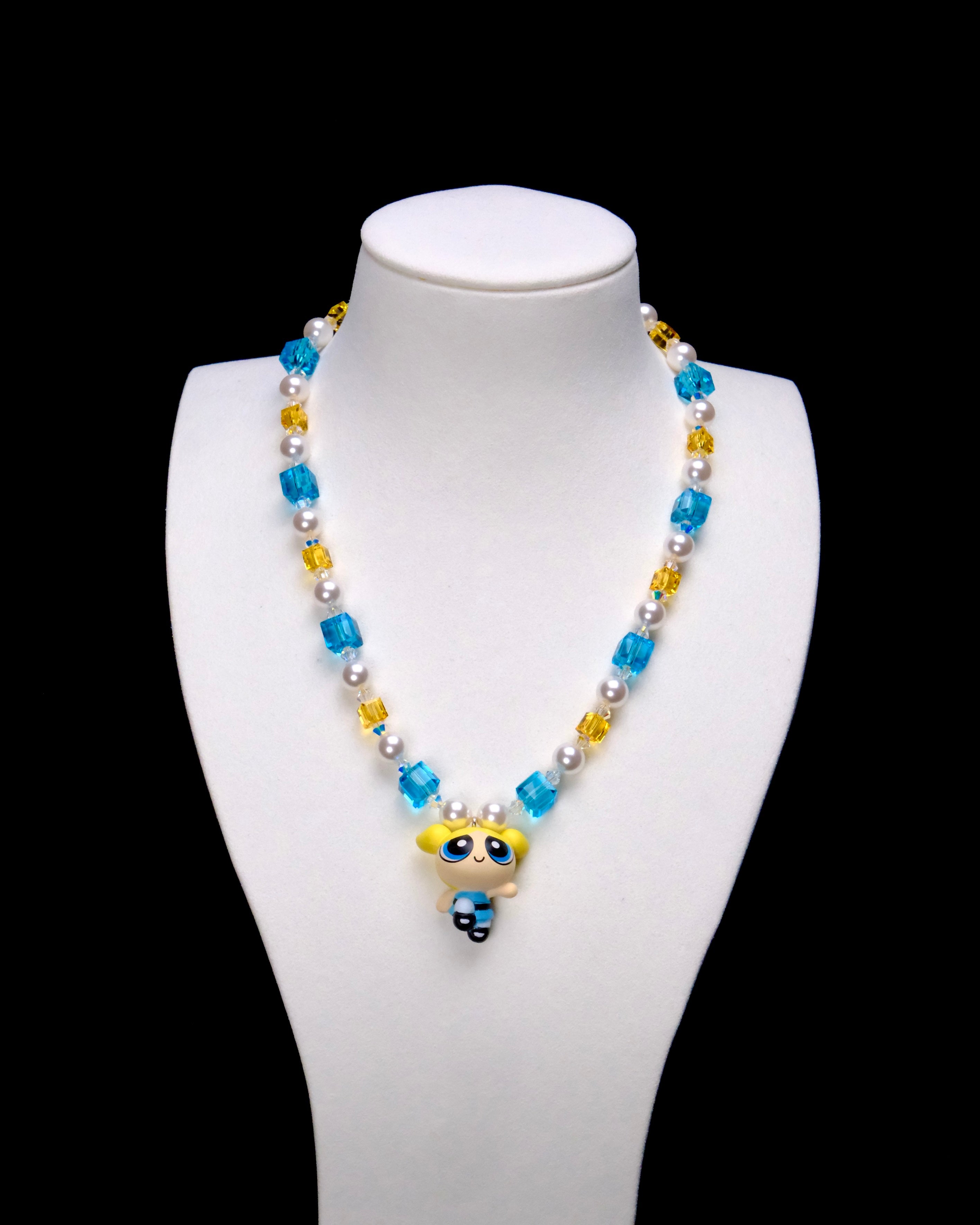Blue Dreamer Charm Necklace with aqua and golden crystal cubes, white pearls and a blonde girl pendant on a white bust.