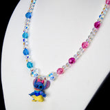 Angled close-up of Blue & Pink Fairytale Charm Necklace showing blue and pink crystals and a blue character in a princess outfit.
