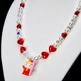 Angled close-up of Ruby Heart Snow Day Charm Necklace showing red heart crystals, white pearls and a red winter-outfit cat pendant.