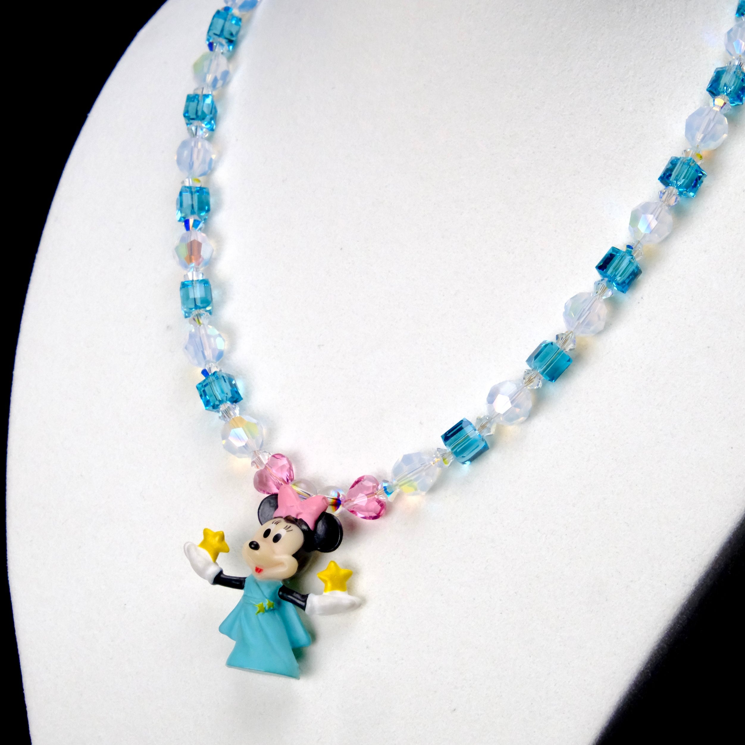 Angled close-up of Aqua Star Wishes Charm Necklace showing aqua crystals, star beads and a pink-bow mouse holding a yellow star.