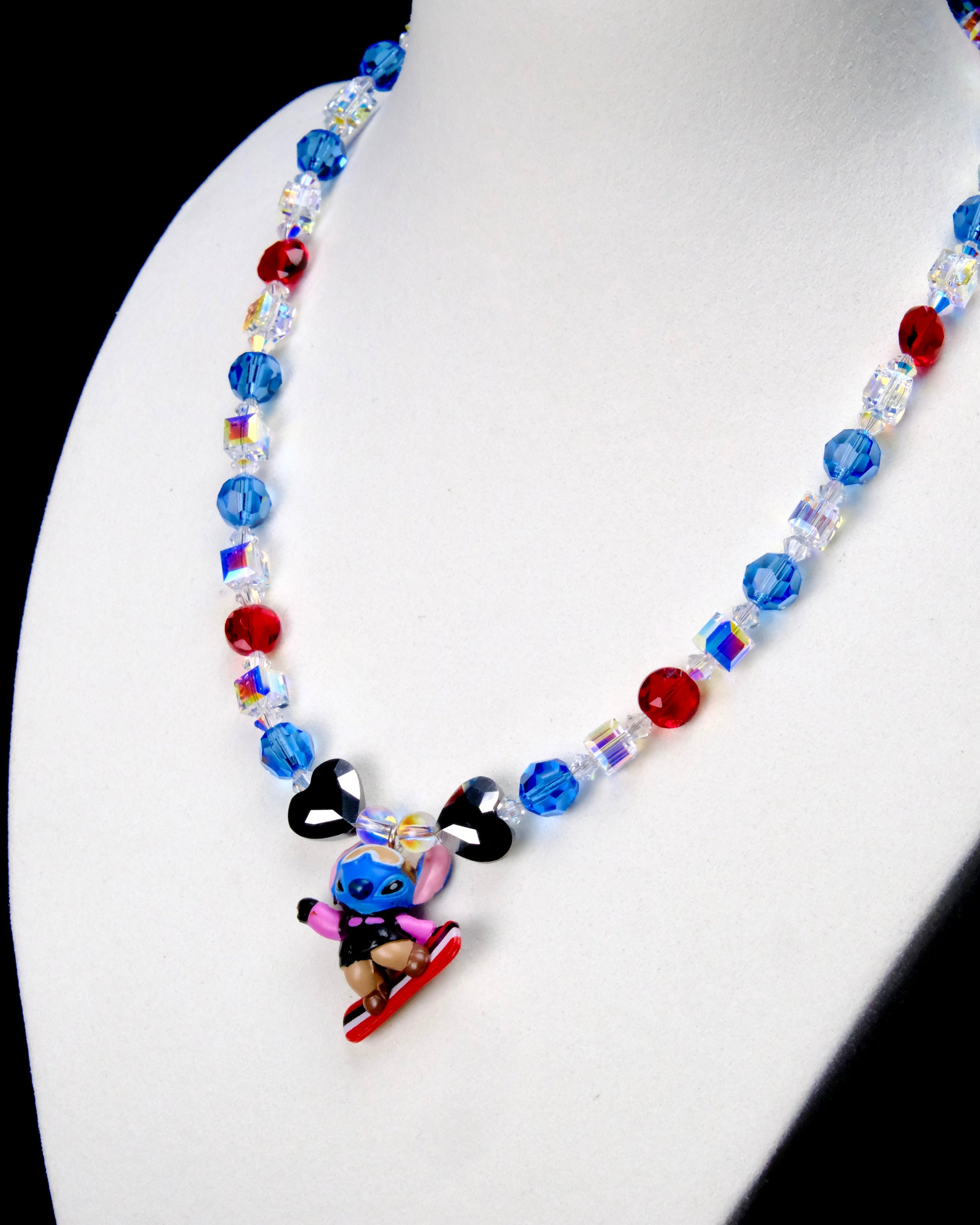 Angled close-up of Blue & Red Board Rider Charm Necklace showing blue and red crystals, black heart beads and a character on a red board.