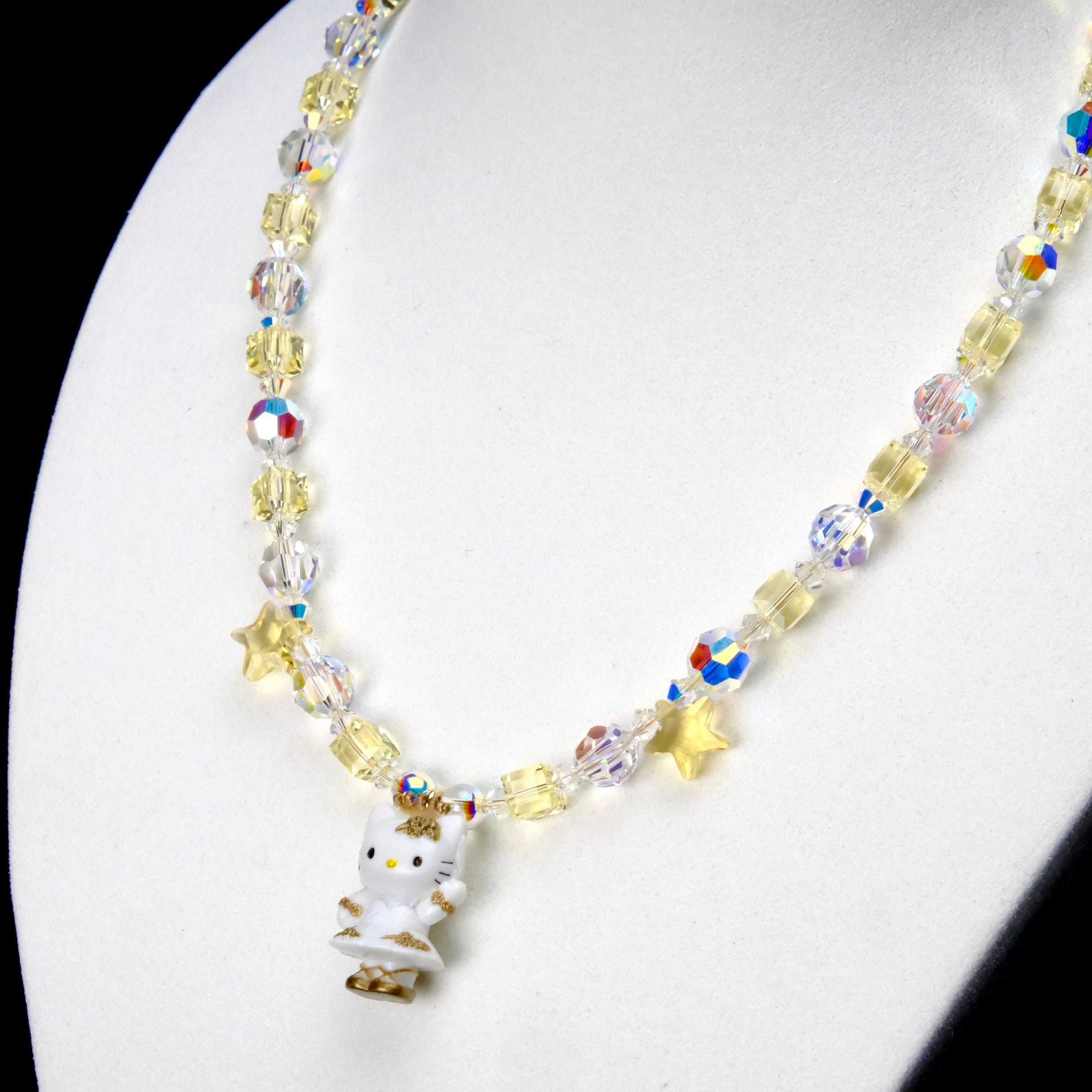 Angled close-up of Golden Star Cat Charm Necklace showing pale yellow crystals, iridescent star beads and a white cat with a gold star.
