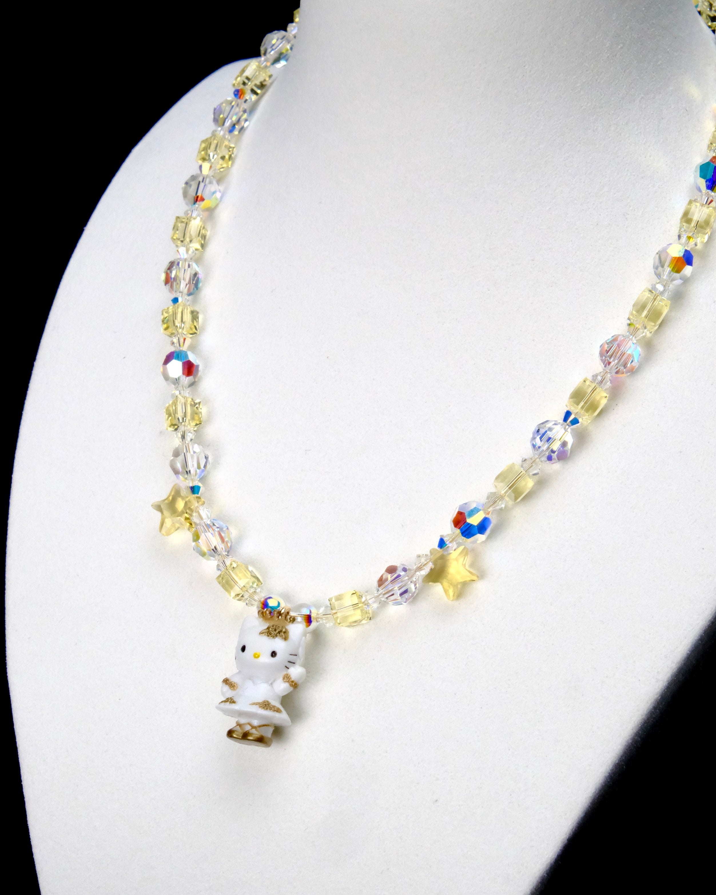 Angled close-up of Golden Star Cat Charm Necklace showing pale yellow crystals, iridescent star beads and a white cat with a gold star.