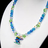 Angled close-up of Ocean Blue Star Rider Charm Necklace showing blue crystals, green star beads and a blue character on a green board.