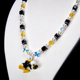 Angled close-up of Black & Gold Melody Charm Necklace showing black and yellow crystals, white pearls and a duck with a brass instrument.