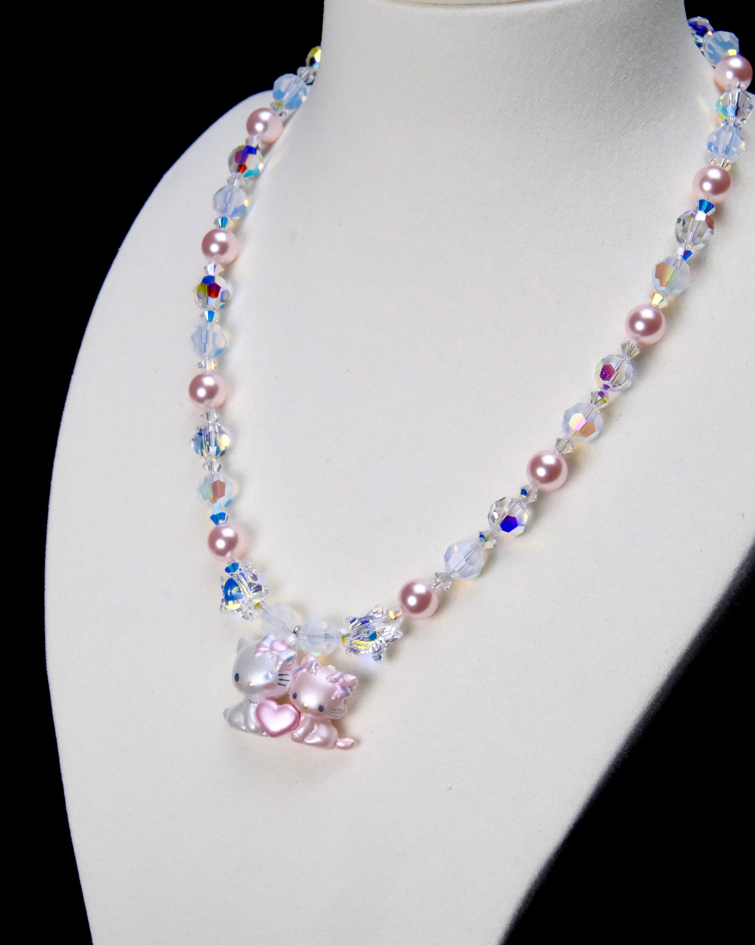 Angled close-up of Sweethearts Cat Duo Necklace showing two cat figures with a pink heart, pink pearls and iridescent crystals.