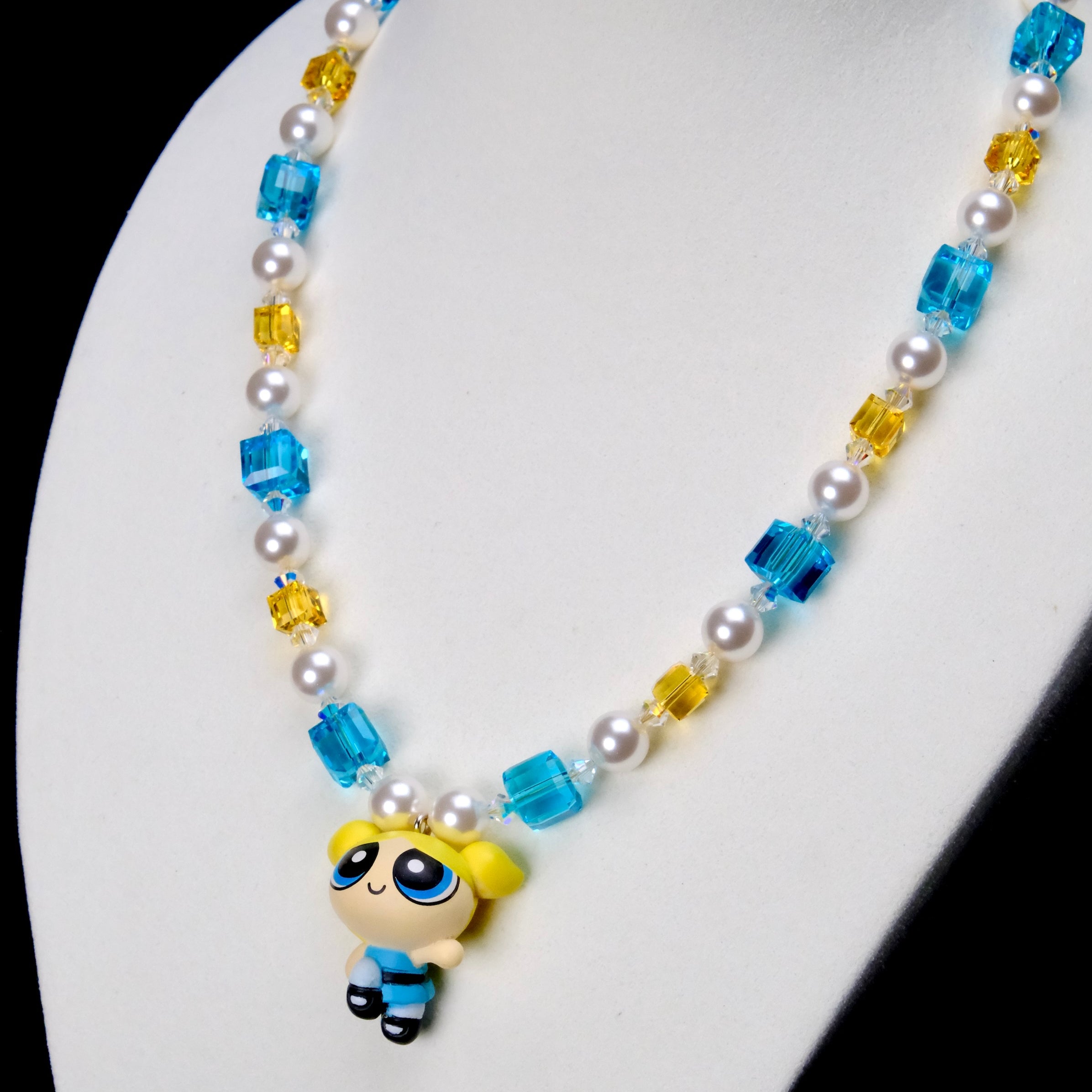 Angled close-up of Blue Dreamer Charm Necklace showing the blue-outfit girl pendant, aqua crystals and white pearls.
